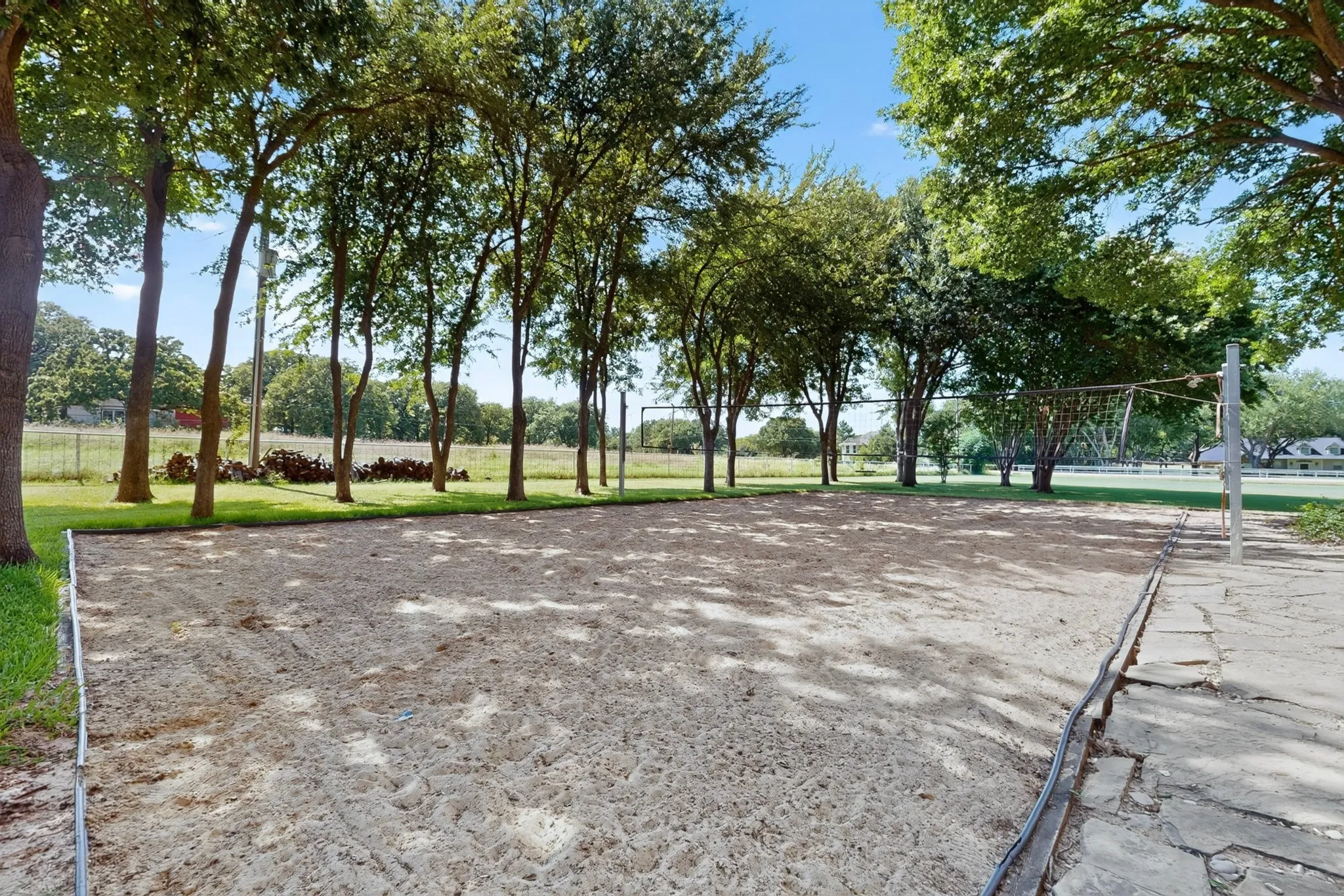 Sand Volleyball court with a net, bordered by mature trees and natural landscaping