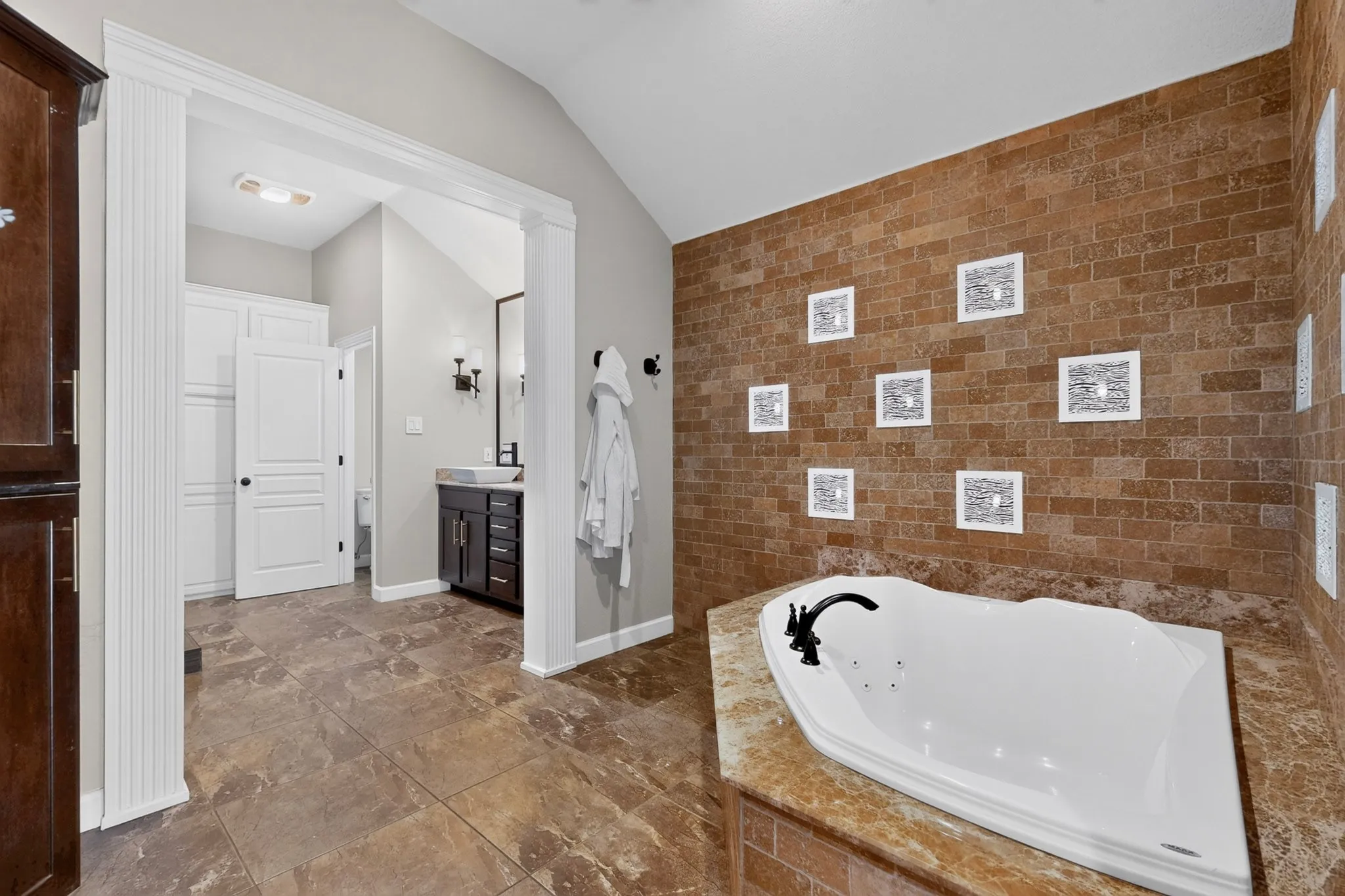 Soaking tub with a matte black faucet, surrounded by a natural stone-look tile and a coordinating wall accent
