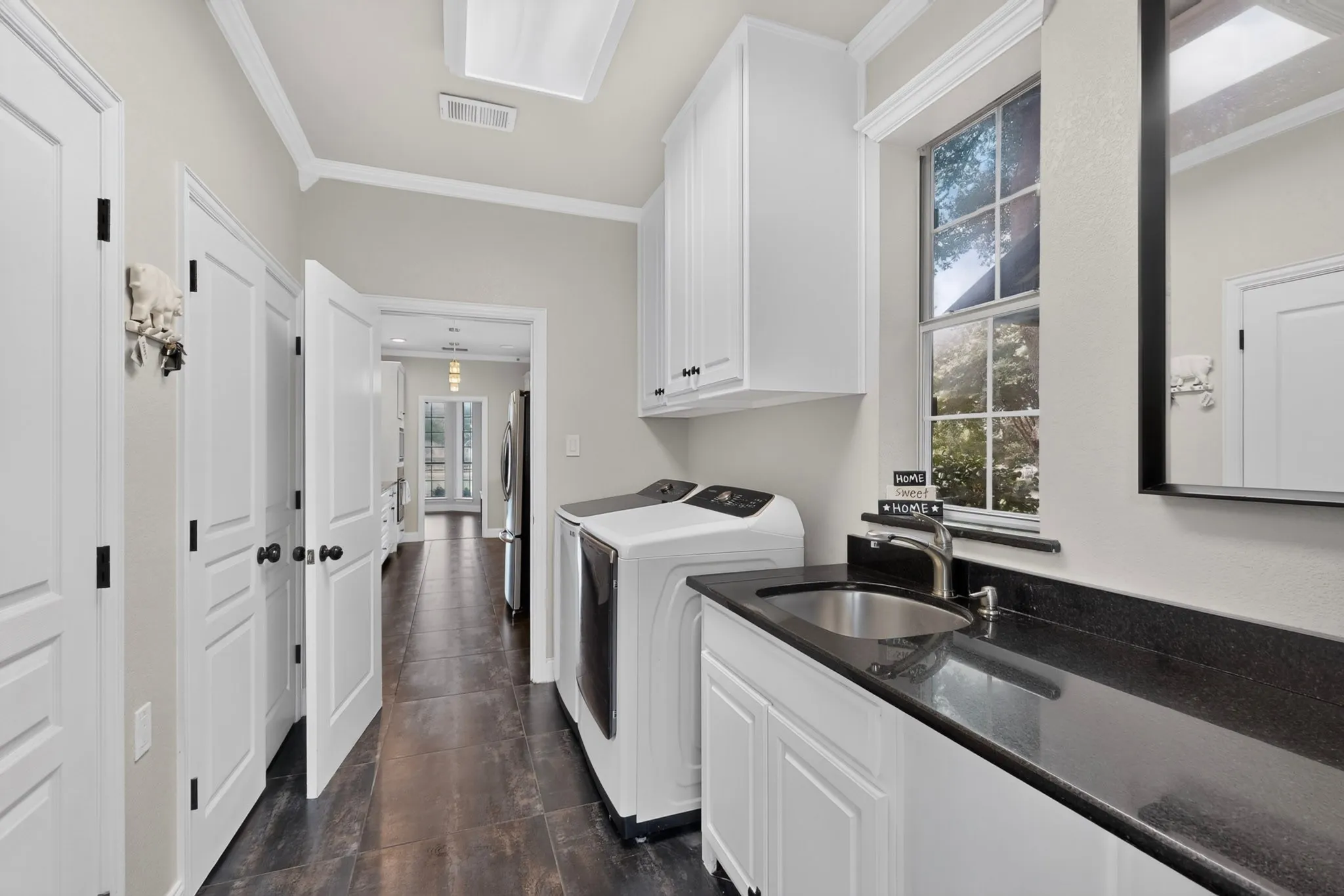 Dedicated utility room featuring dark wood-finish flooring, white cabinetry, a dark countertop, and an undermount sink