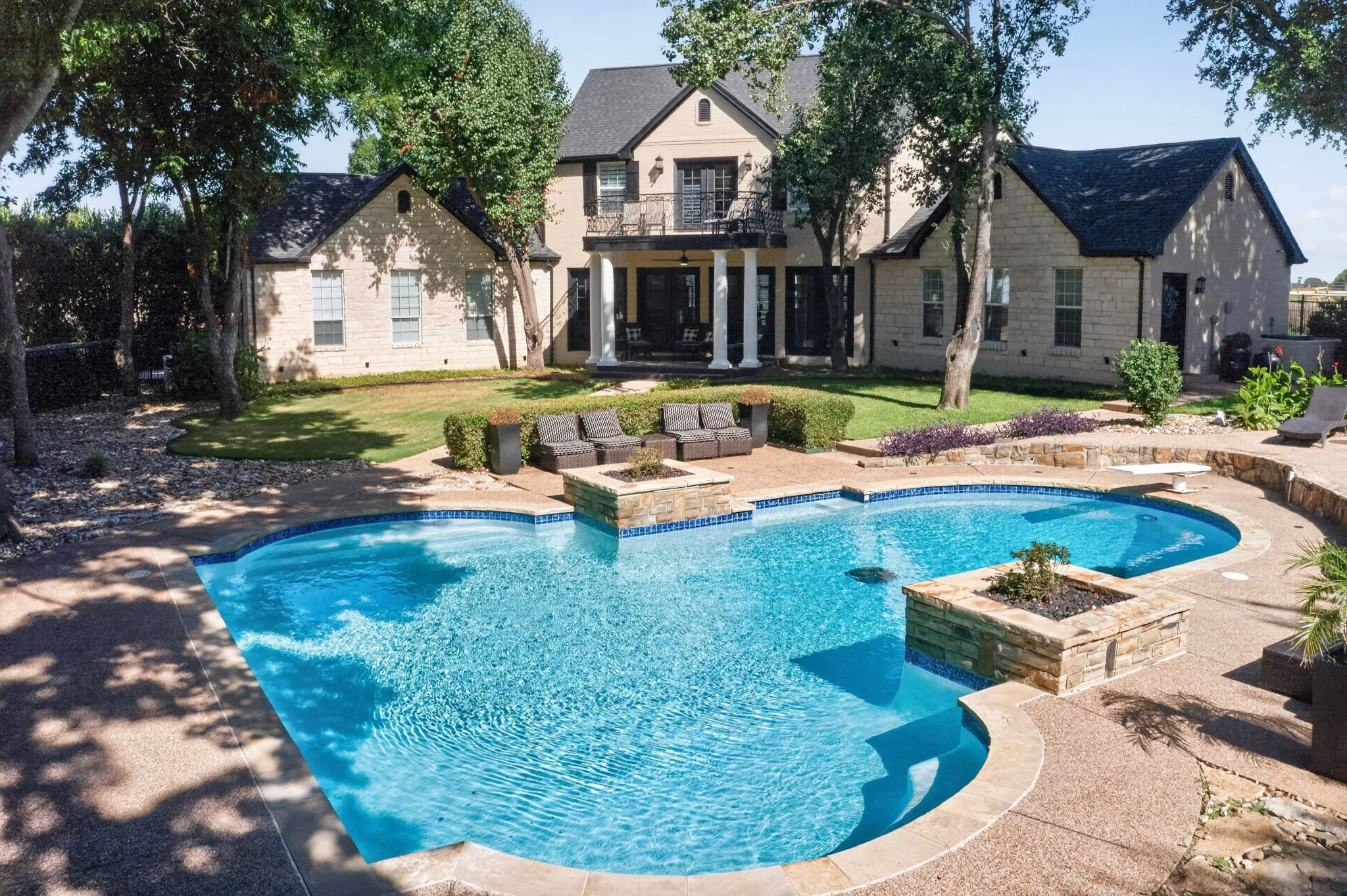Expansive backyard with a freeform pool featuring a diving board, integrated planters with stone surrounds, and a wide-set concrete deck
