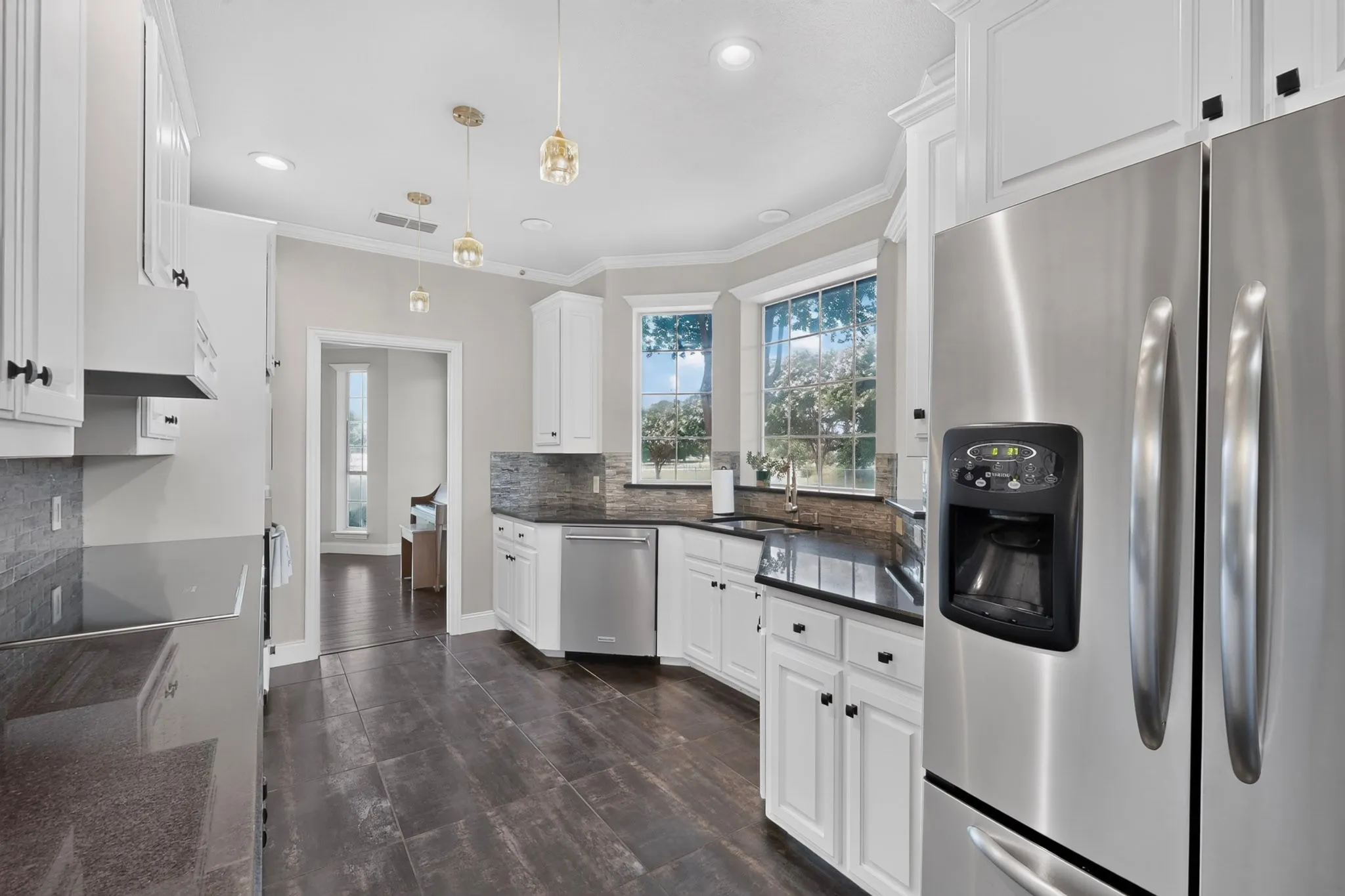 Kitchen featuring stainless steel appliances, white cabinetry with black hardware, dark wood-finish flooring, and a stone backsplash