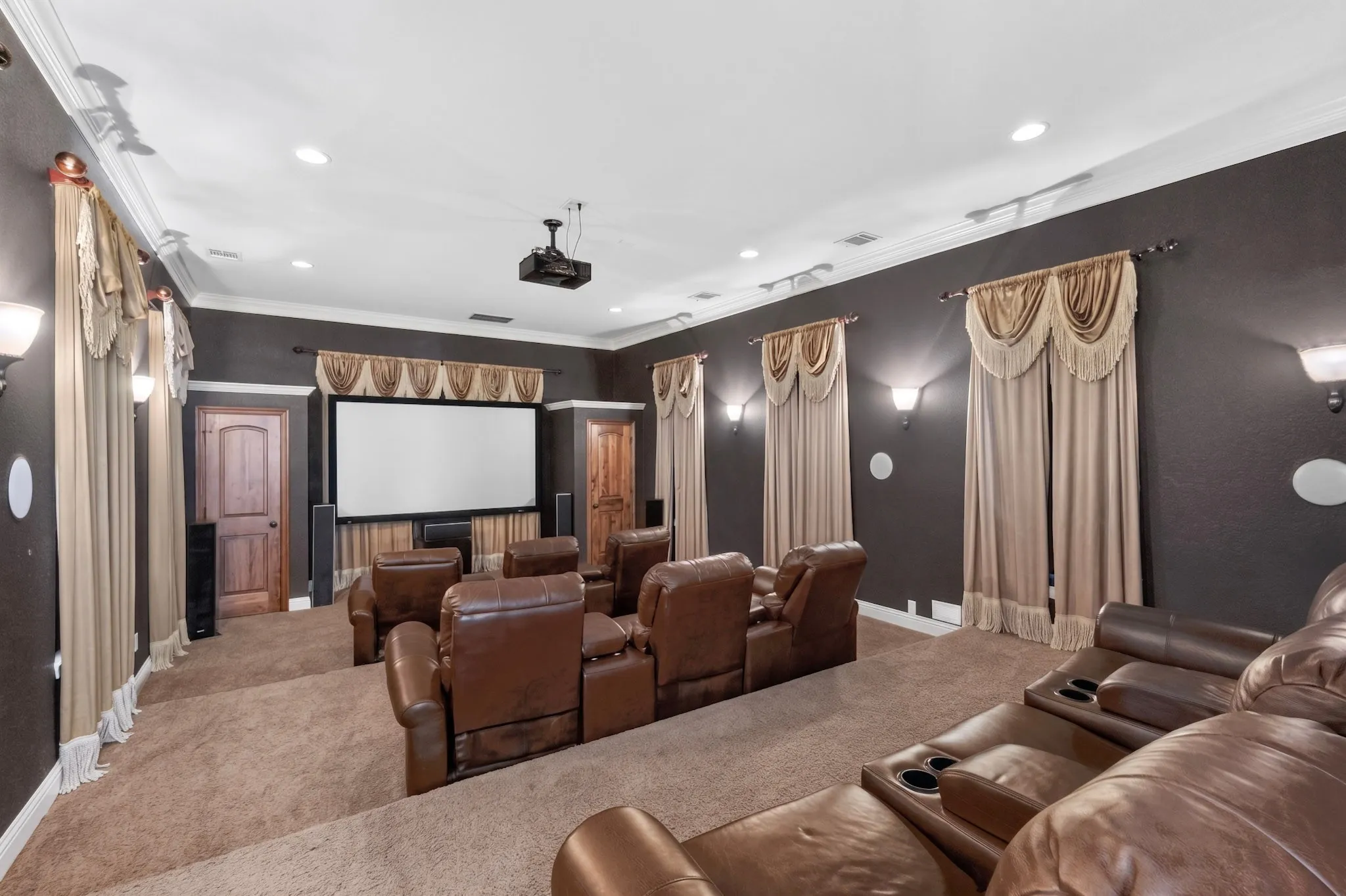 Dedicated media room featuring tiered seating, a large projection screen, a ceiling-mounted projector, wall sconces, and recessed lighting
