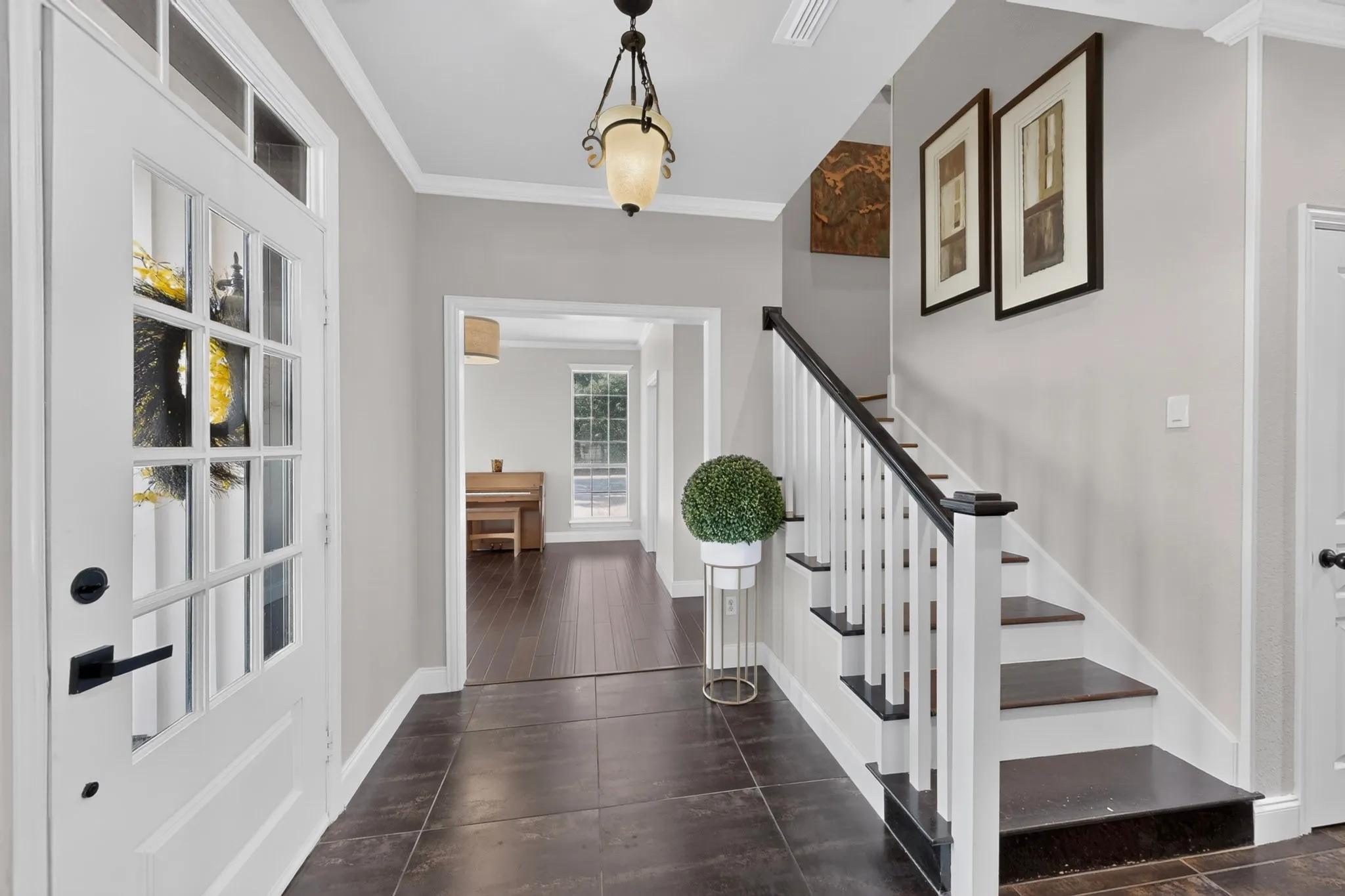 Foyer featuring dark tile flooring, a staircase with white risers and dark wood-finish treads, a white paneled front door with multiple lites, and a decorative ceiling light fixture