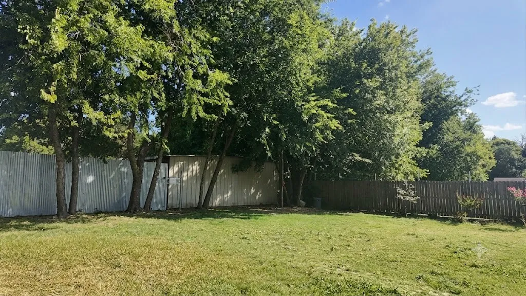 Expansive grassy yard featuring mature trees and a corrugated metal fence
