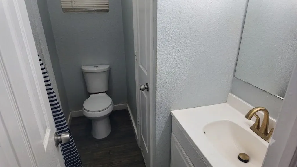 Compact bathroom featuring a white vanity with an integrated sink, gold-tone faucet, and a wall-mounted mirror