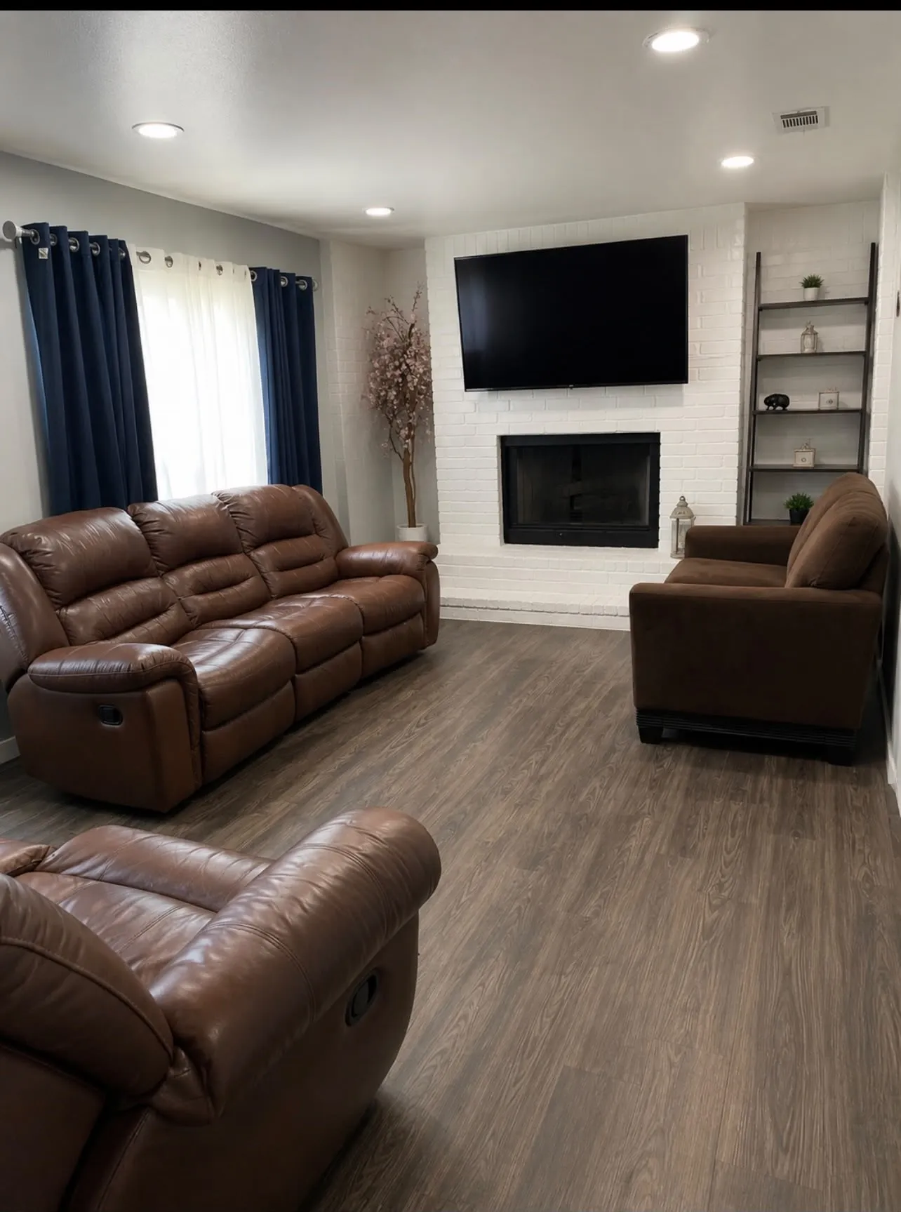 Spacious living area featuring wood-finish flooring, recessed lighting, and a white brick fireplace