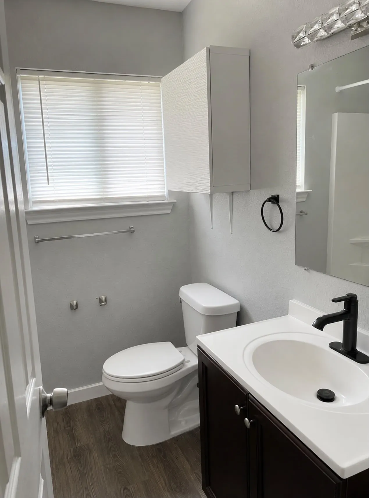 Bathroom featuring a dark wood-finish vanity with an integrated white sink, a modern black faucet, and wood-finish flooring