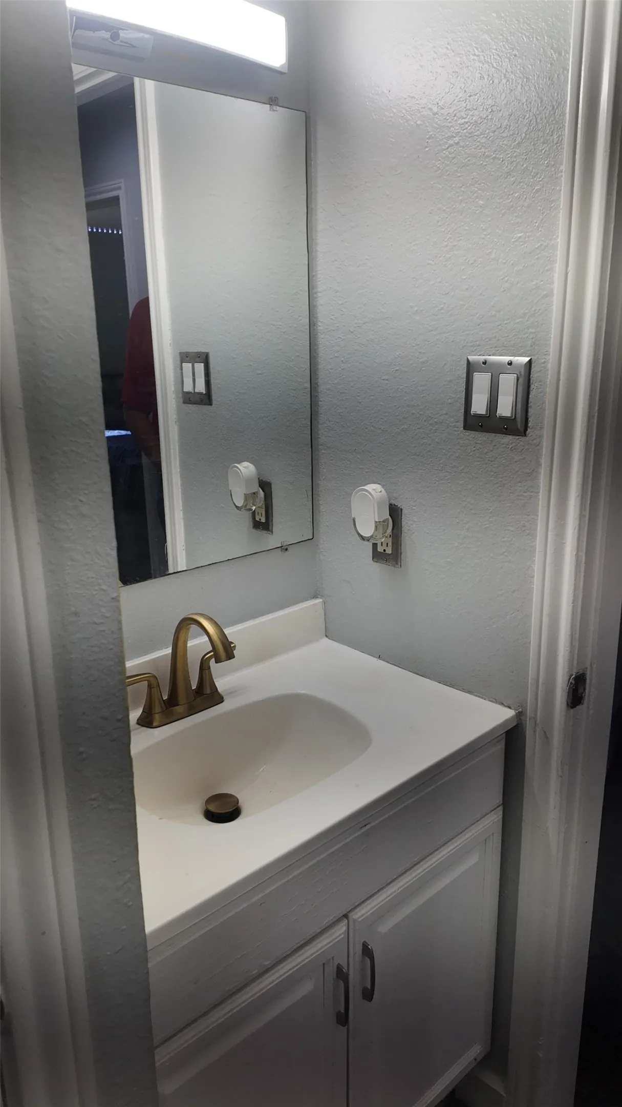 Bathroom vanity featuring a white countertop with an integrated sink, a bronze-finish faucet, and coordinating white cabinetry with dark pulls