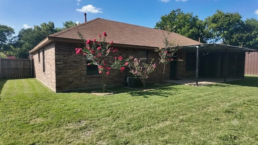 Rear exterior featuring a brick facade, shingle roof, and an expansive covered patio