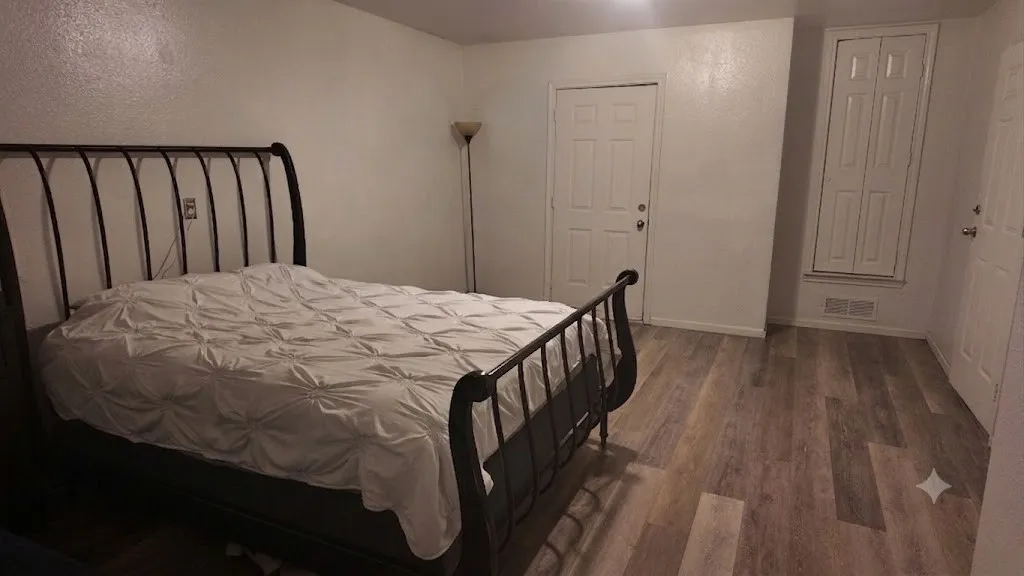Spacious room featuring wood-finish flooring, white walls, and multiple panel doors