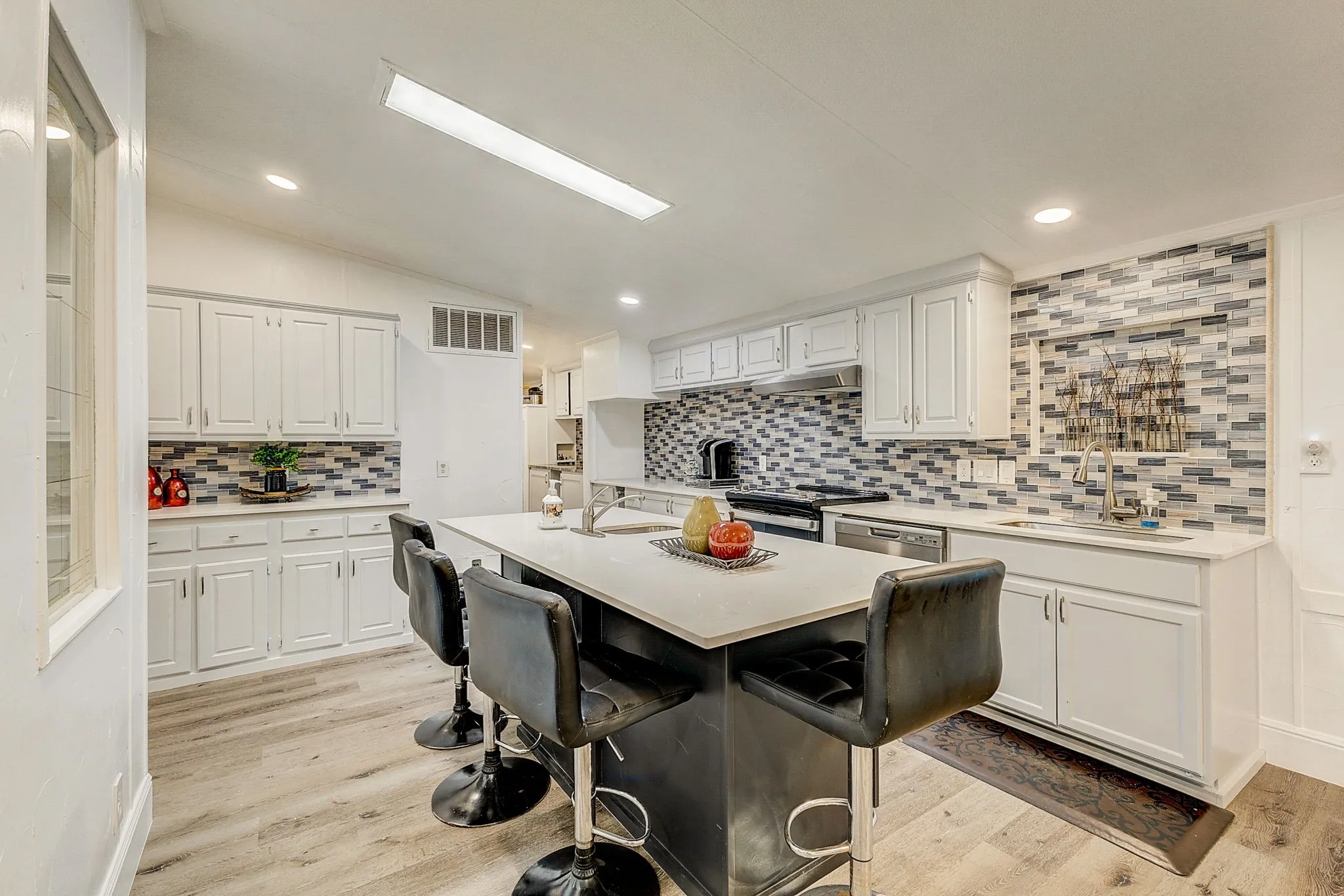 Kitchen with designer backsplash, quartz countertops,  wood-style flooring, stove, white cabinets, and stainless steel appliances and quartz countertop  Island with stainless steel sink.