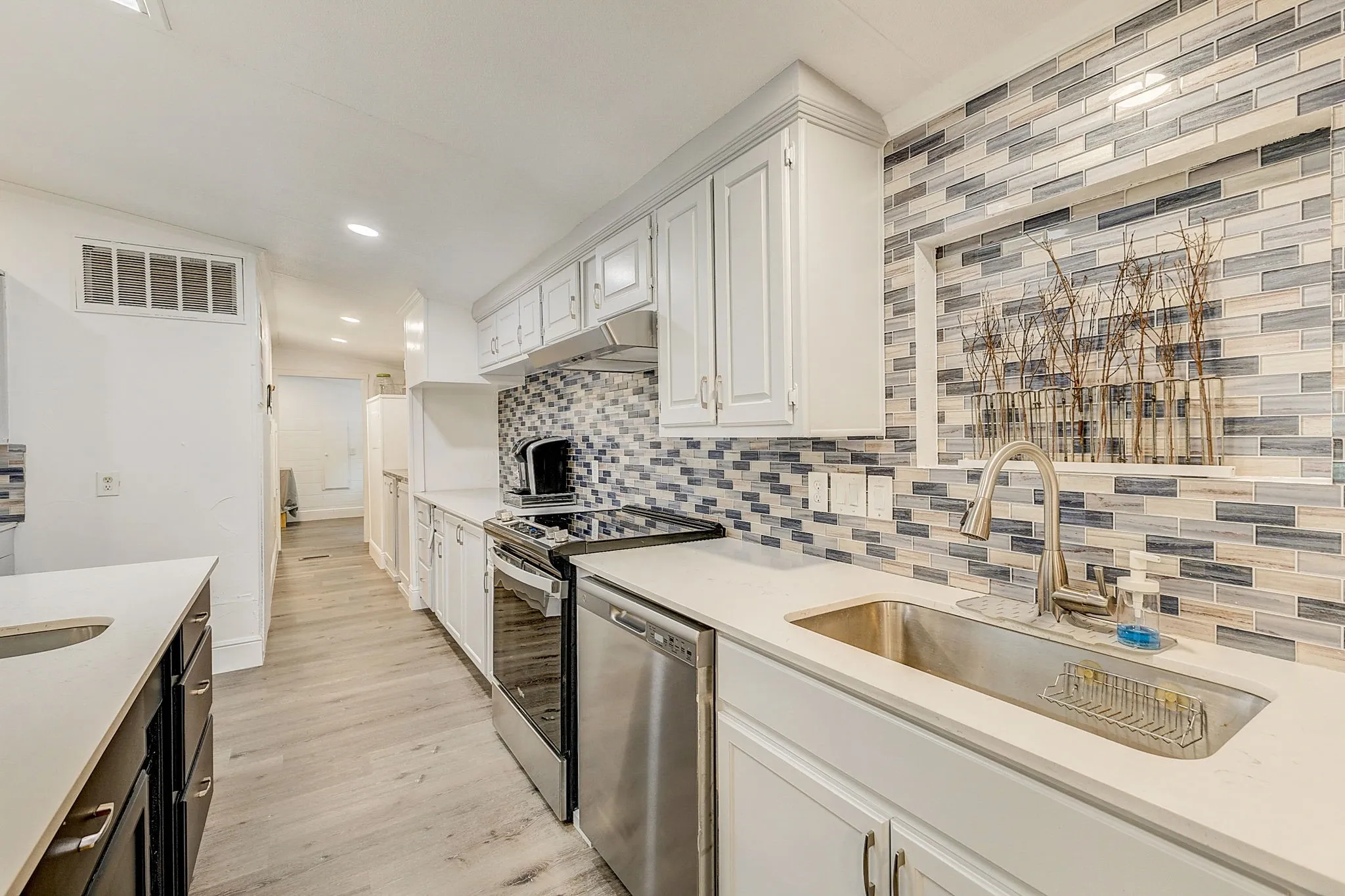 Kitchen with designer backsplash, quartz countertops,  wood-style flooring, stove, white cabinets, and stainless steel appliances and quartz countertop  Island with stainless steel sink.