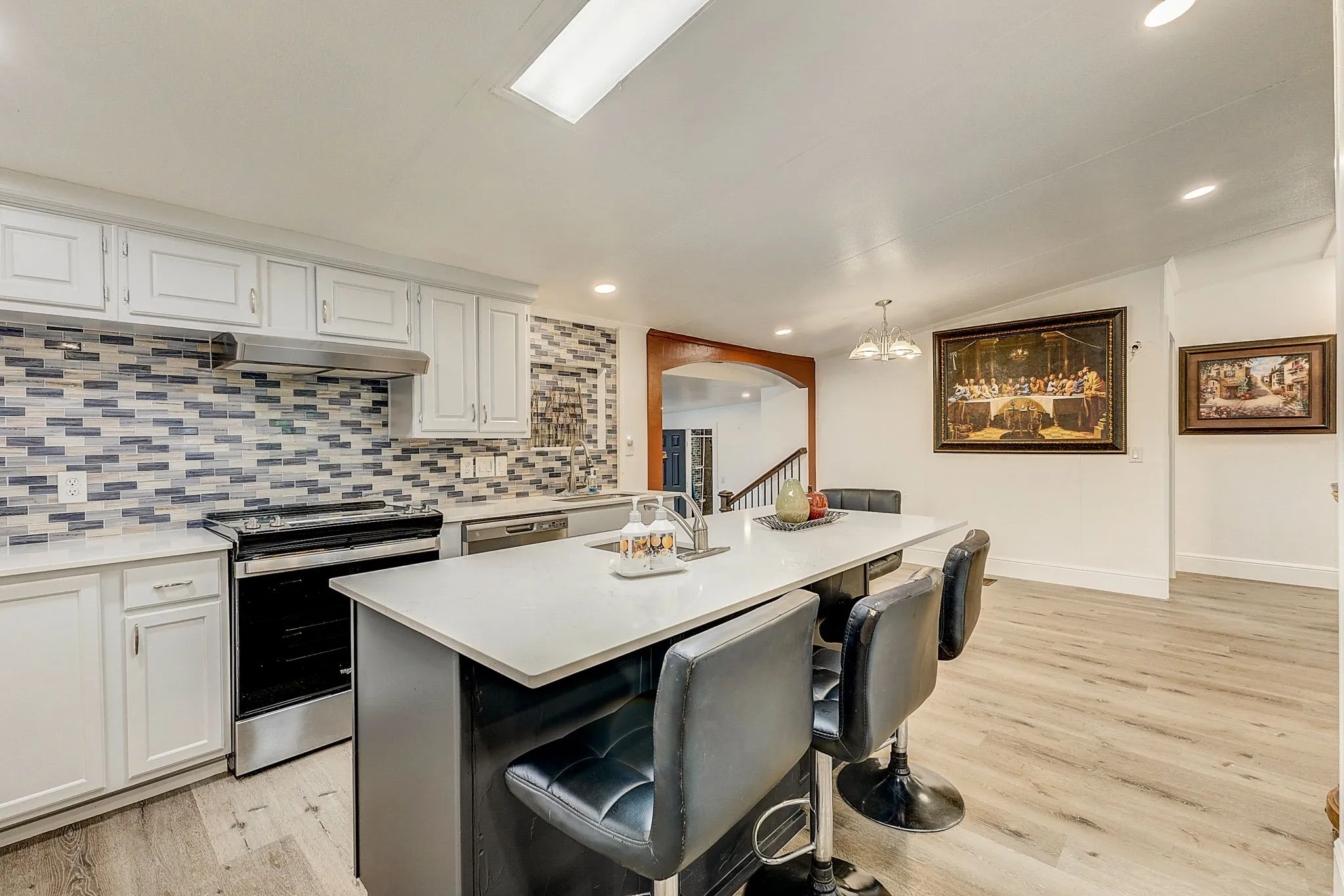 Kitchen with designer backsplash, quartz countertops,  wood-style flooring, stove, white cabinets, and stainless steel appliances and quartz countertop  Island with stainless steel sink.