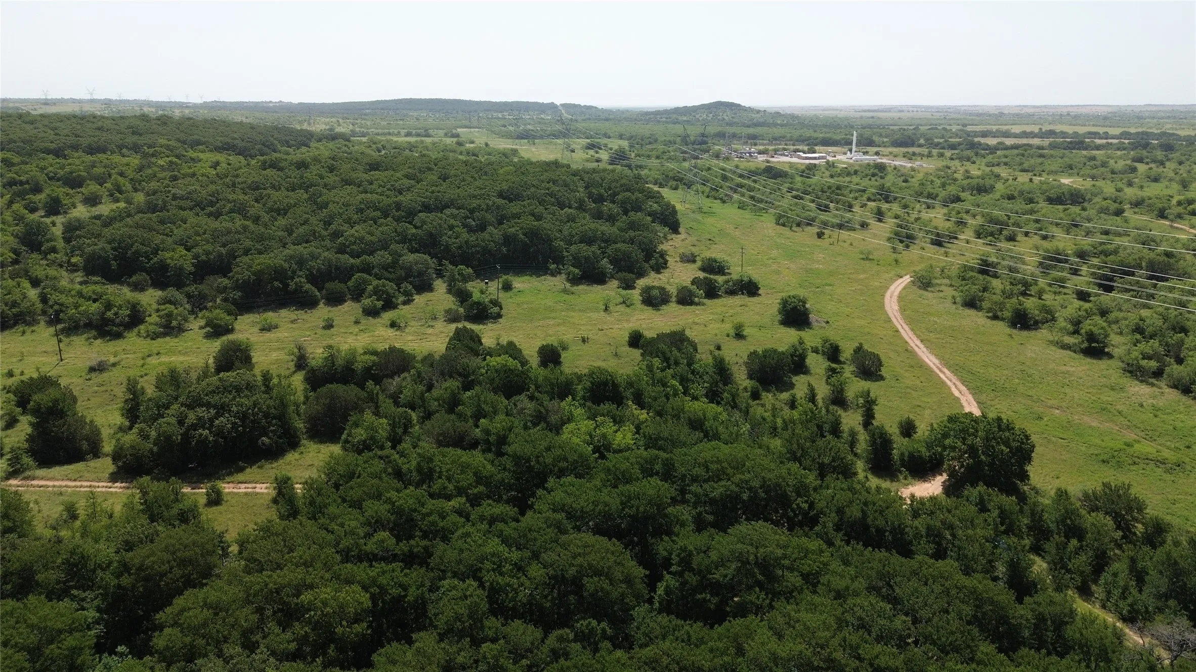 Expansive land parcel featuring dense tree coverage, open grassy areas, and a visible dirt road