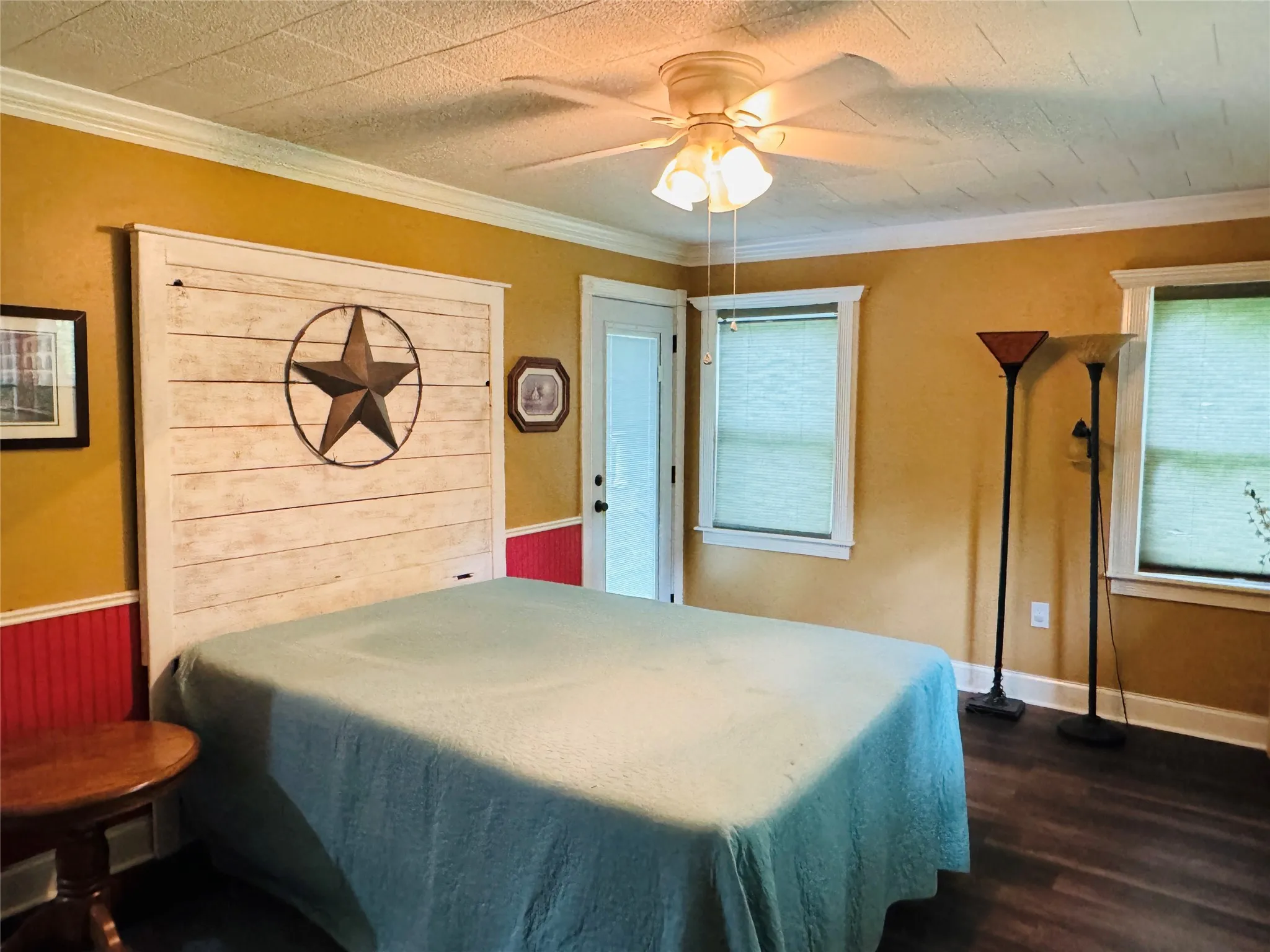 Primary Bedroom featuring a custom wainscoted wall, crown molding, a ceiling fan, and dark wood-style flooring