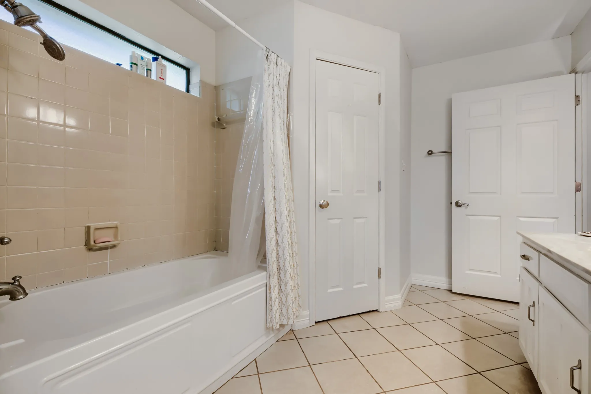 Bathroom featuring a built-in tub with a beige tile surround, a transom window, and a shower fixture