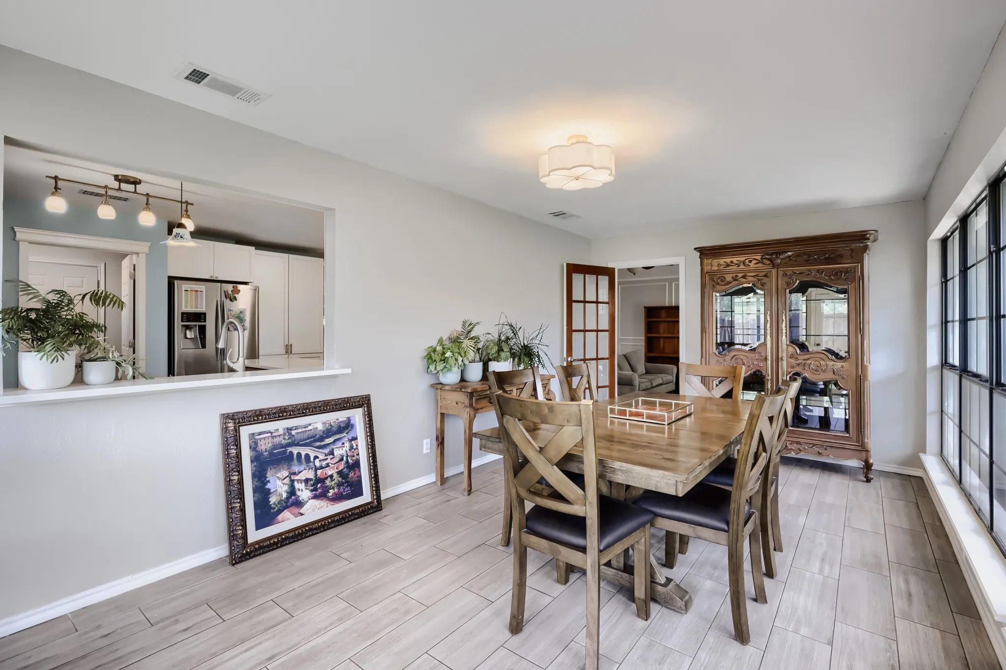 Spacious dining area featuring wood-finish flooring, a kitchen pass-through, a large multi-pane window, and French doors
