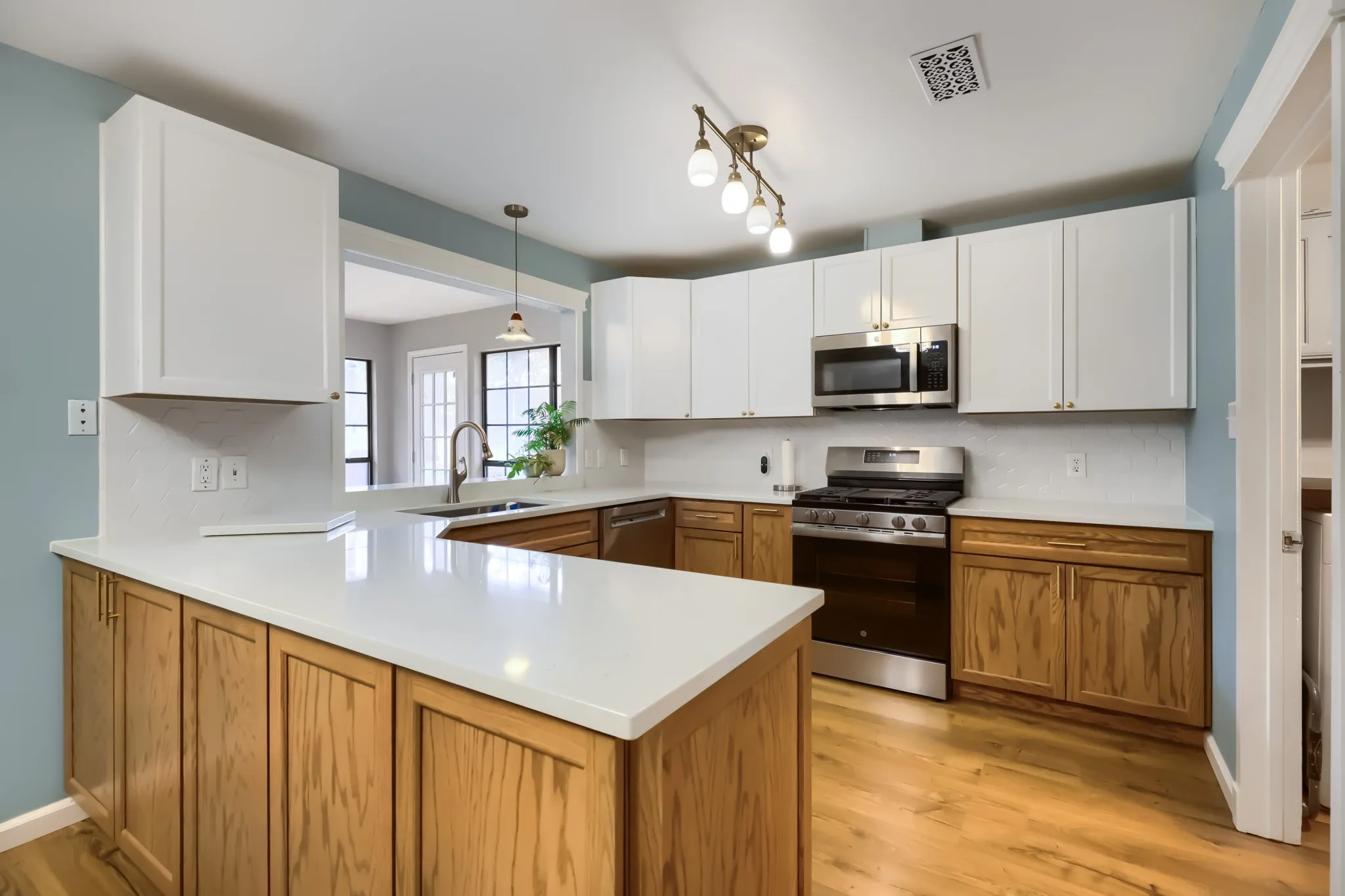 Modern kitchen featuring a peninsula with white countertops, white upper cabinetry, natural wood-finish lower cabinetry, and stainless steel appliances