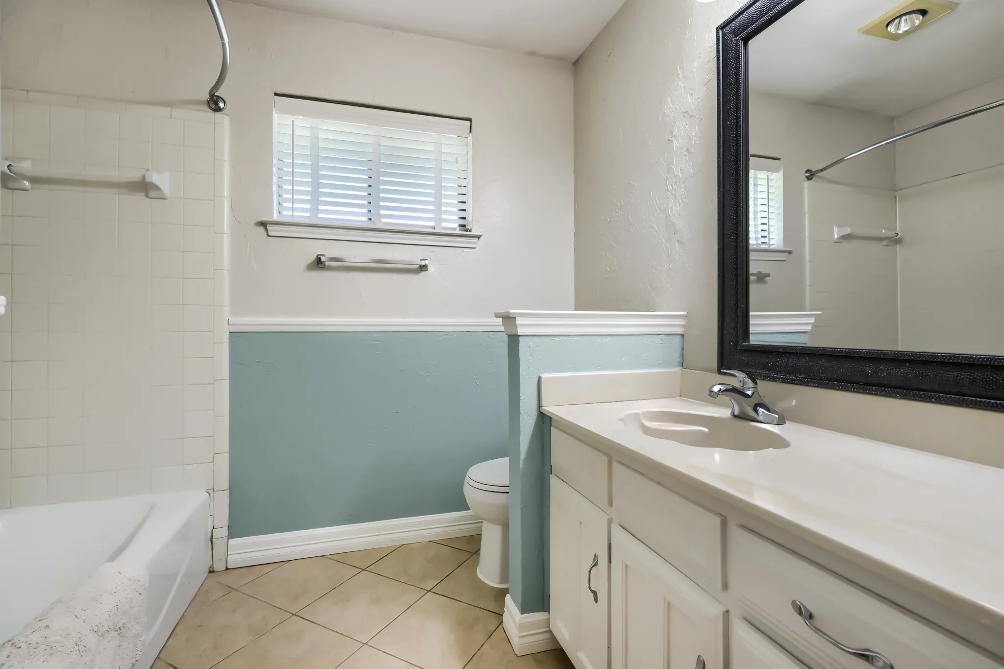 Bathroom featuring a vanity with an integrated sink and chrome faucet, a large framed mirror, and a white bathtub with tiled surround
