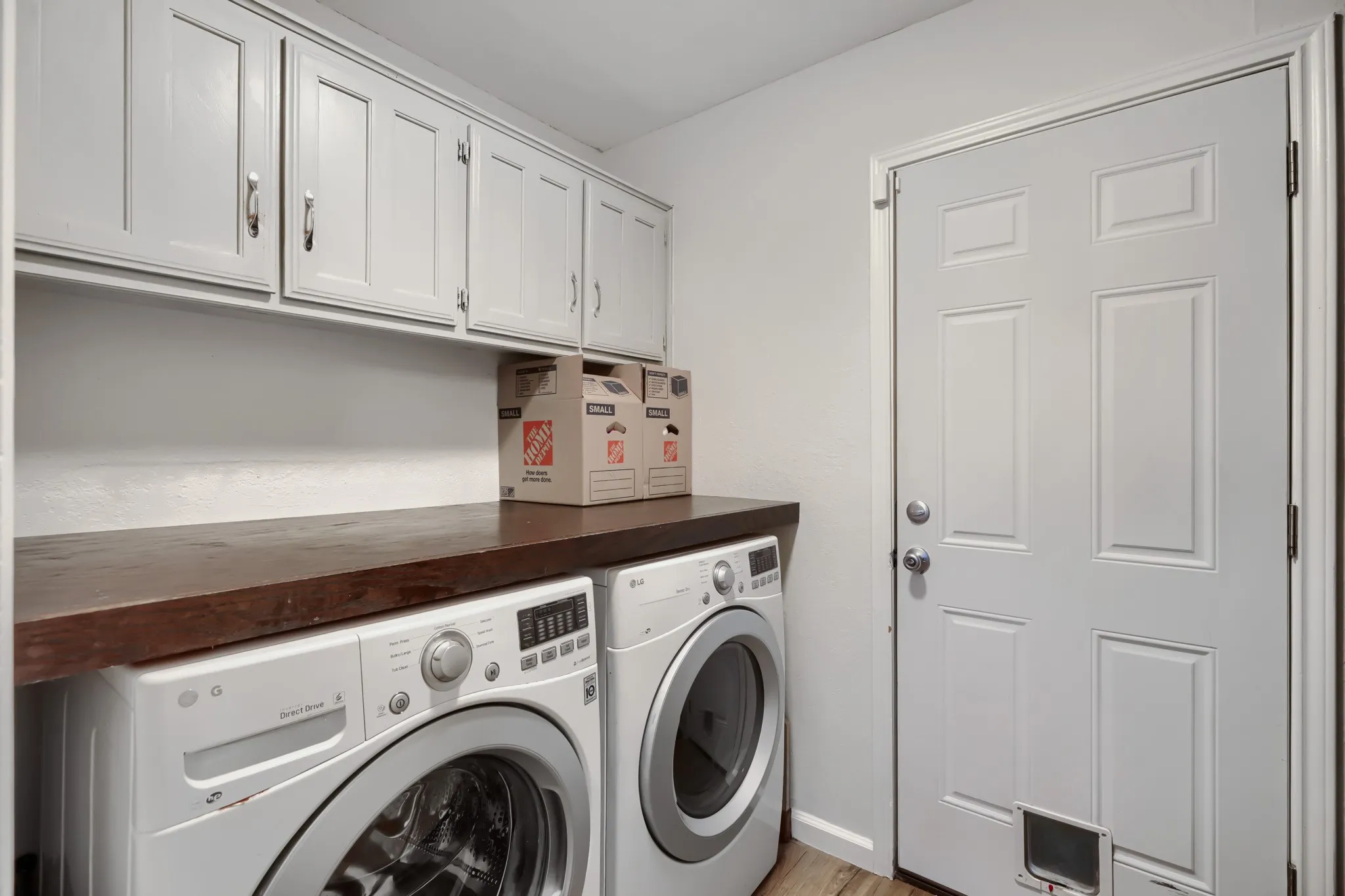 Laundry area featuring white cabinetry with brushed nickel pulls, a dark wood-finish countertop, and light wood-finish flooring