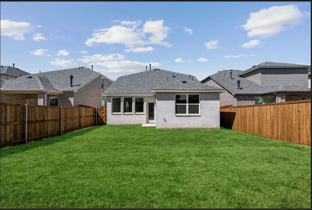 Rear view of property with a fenced backyard, brick siding, and roof with shingles