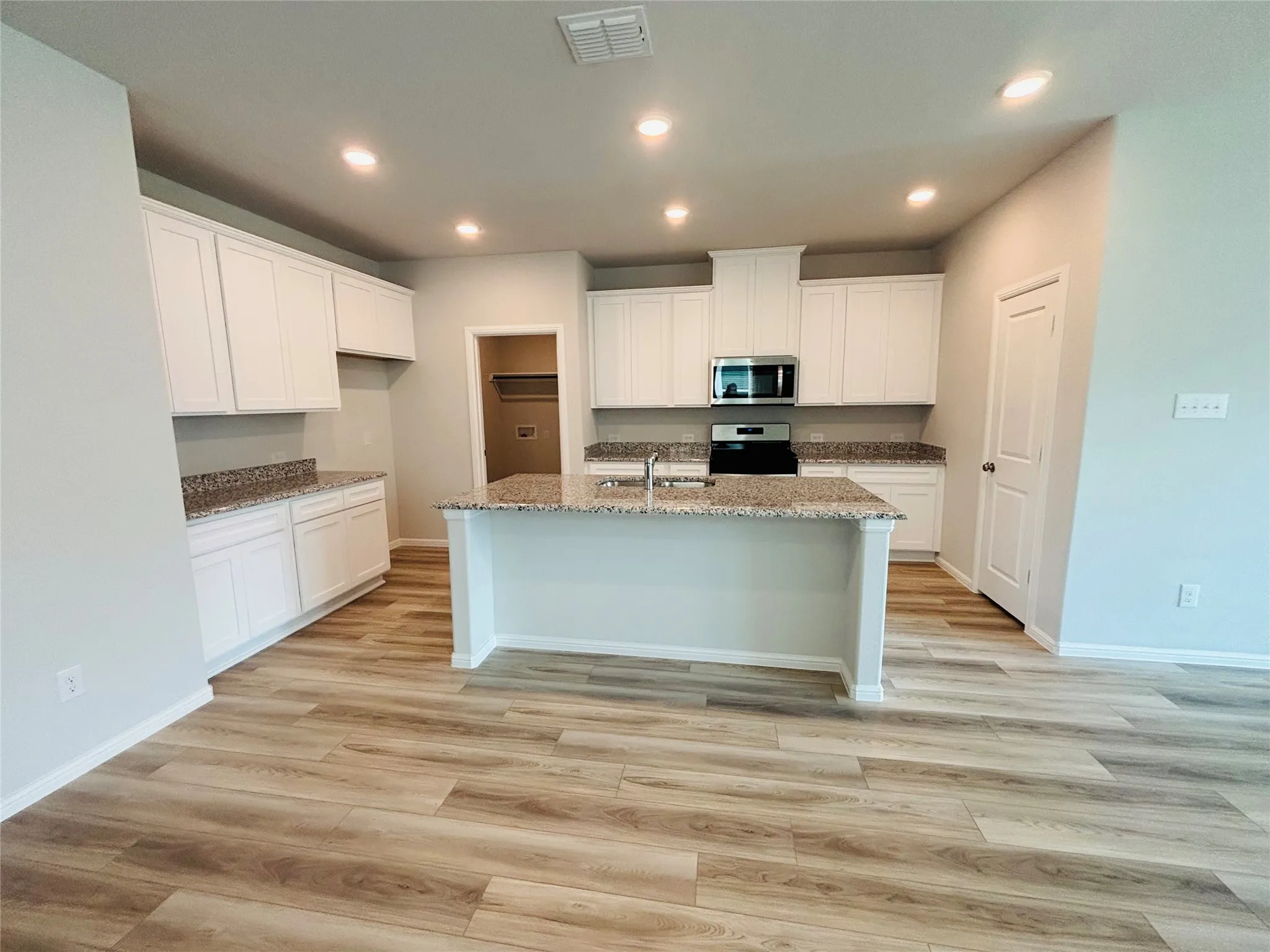 Kitchen with stainless steel microwave, stove, light stone counters, an island with sink, and light wood-type flooring