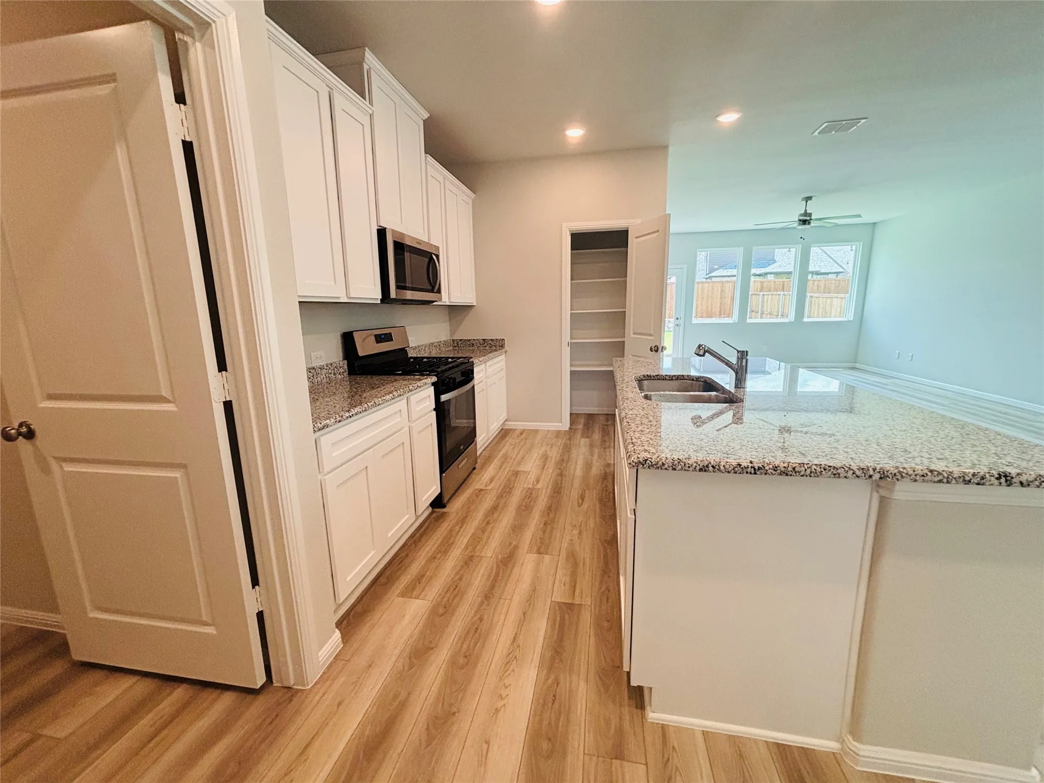 Kitchen featuring appliances with stainless steel finishes, light wood finished floors, white cabinets, a kitchen island with sink, and a ceiling fan