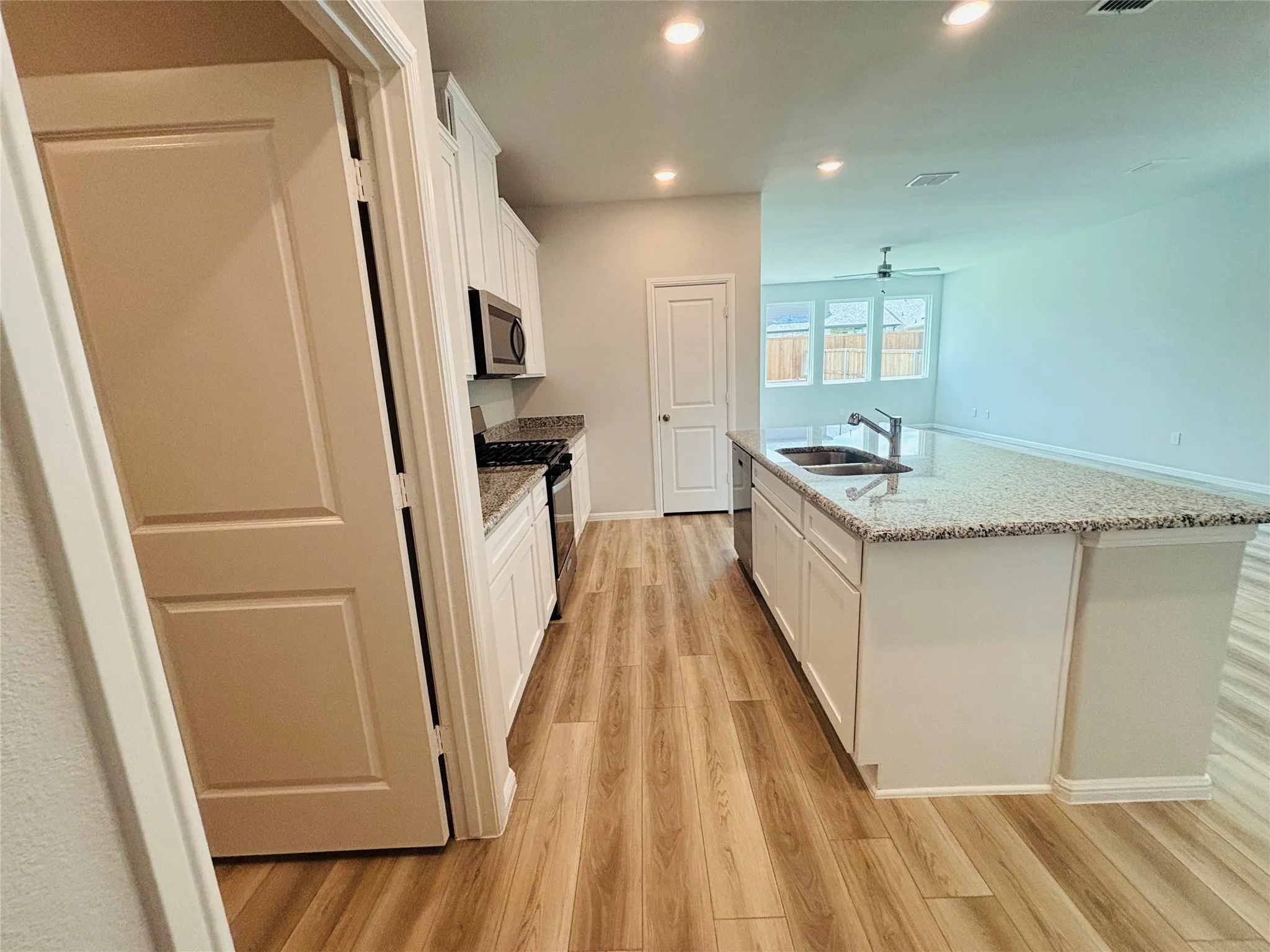 Kitchen with appliances with stainless steel finishes, light wood-style floors, white cabinetry, recessed lighting, and a center island with sink