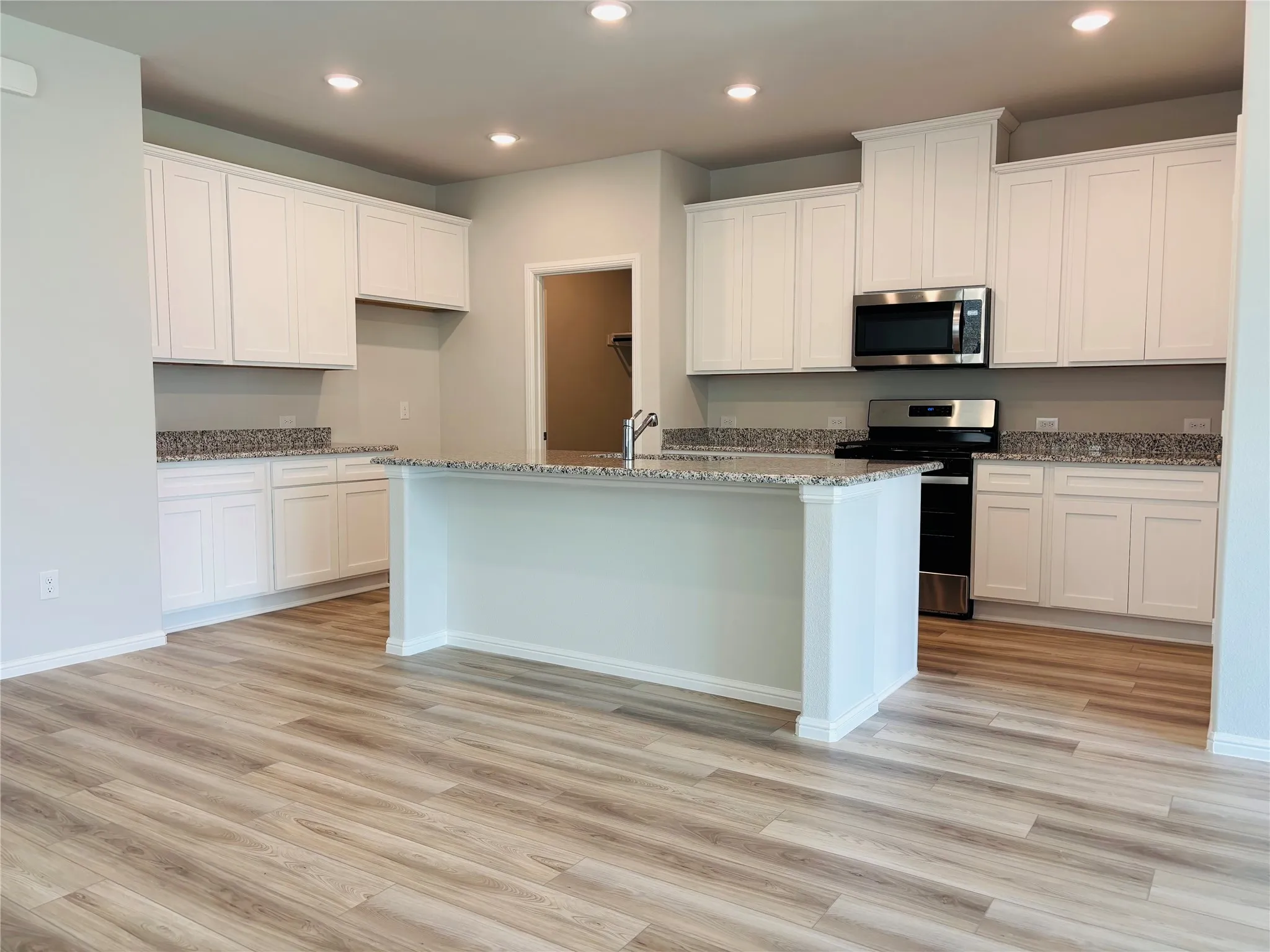 Kitchen featuring stainless steel appliances, light wood-type flooring, recessed lighting, an island with sink, and light stone countertops