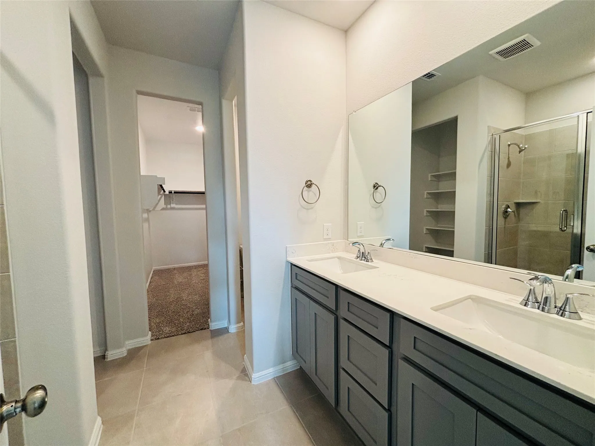 Bathroom featuring a walk in closet, double vanity, a stall shower, and tile patterned flooring
