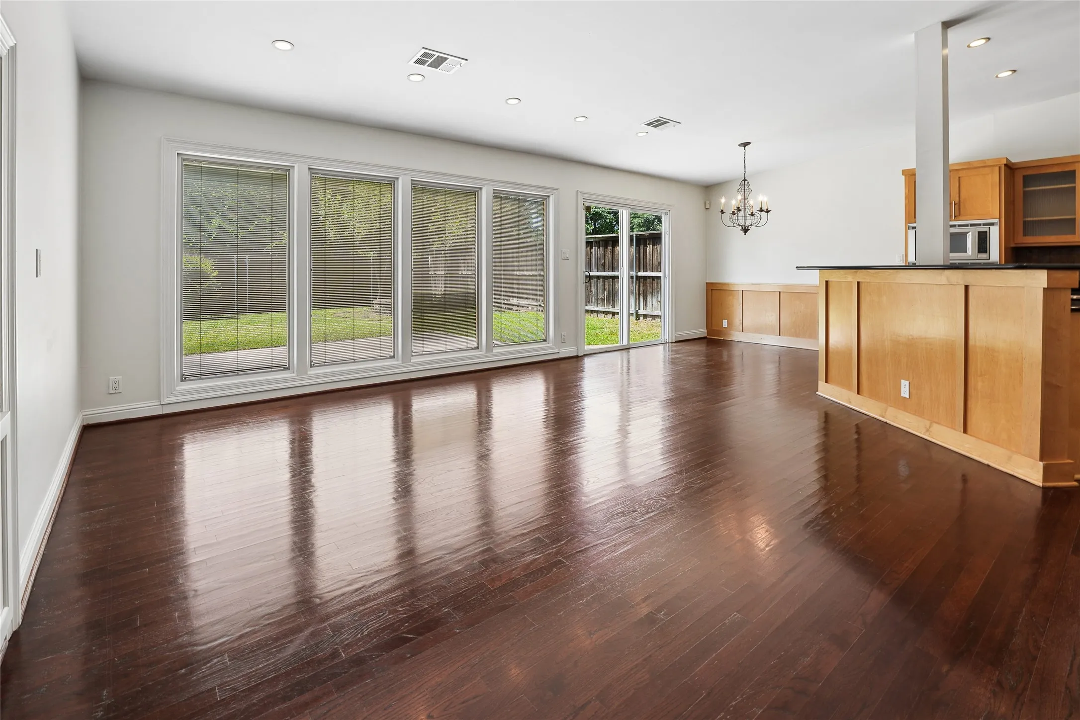 Spacious open-concept room featuring rich wood-finish flooring, recessed lighting, and a chandelier