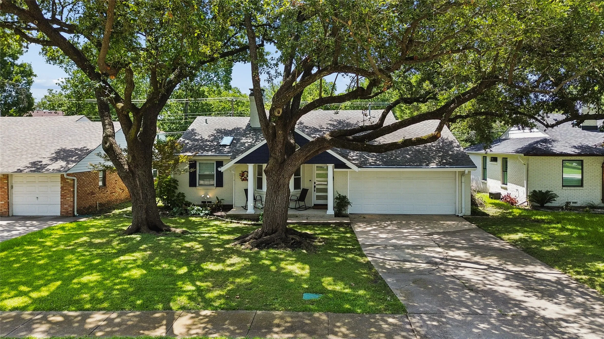 Charming residence featuring a white exterior with dark shutters, a front entry porch, and a two-car garage