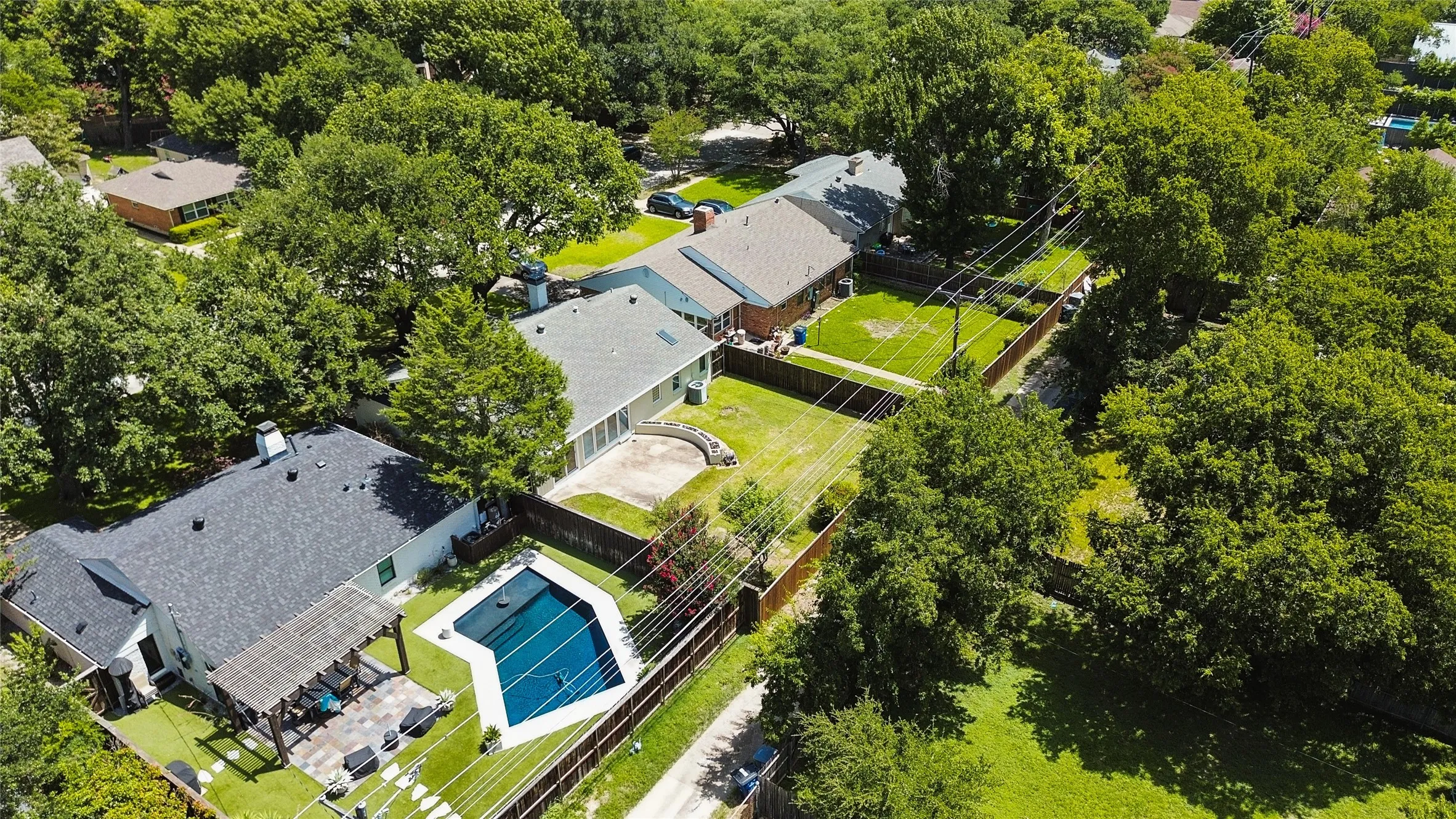 Backyard oasis featuring a geometric swimming pool with white coping, a covered patio area with a pergola, and artificial turf surrounding the pool deck