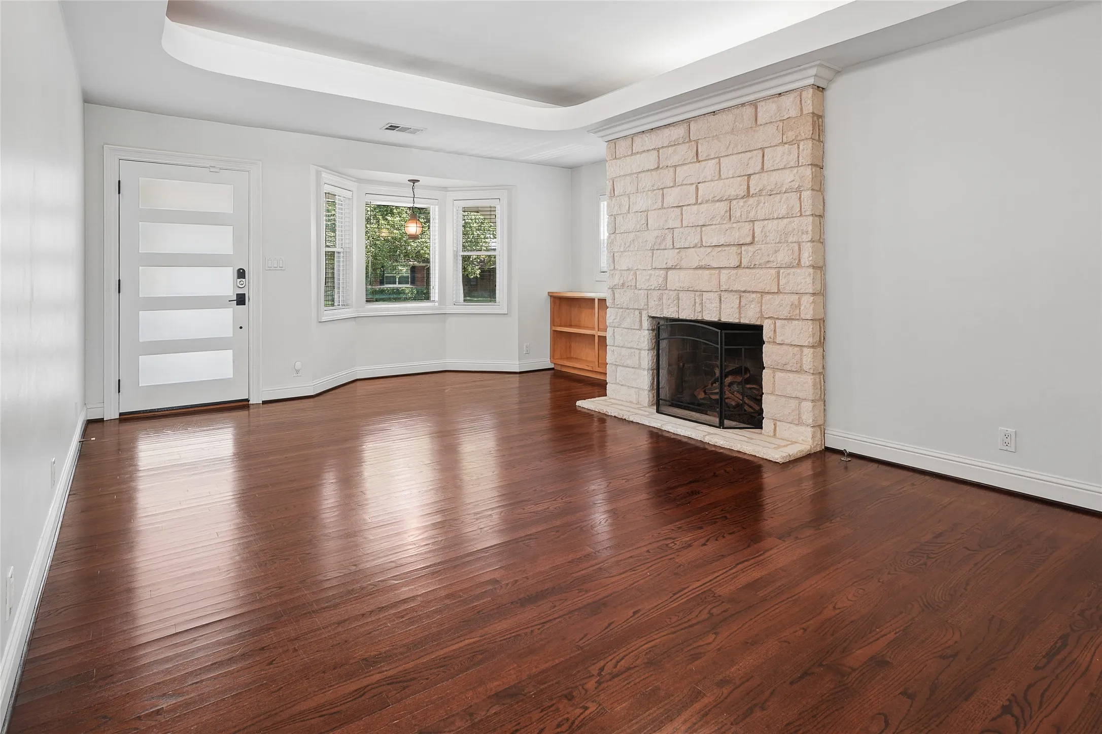 Spacious interior featuring rich wood-finish flooring and a stone fireplace with a black metal grate