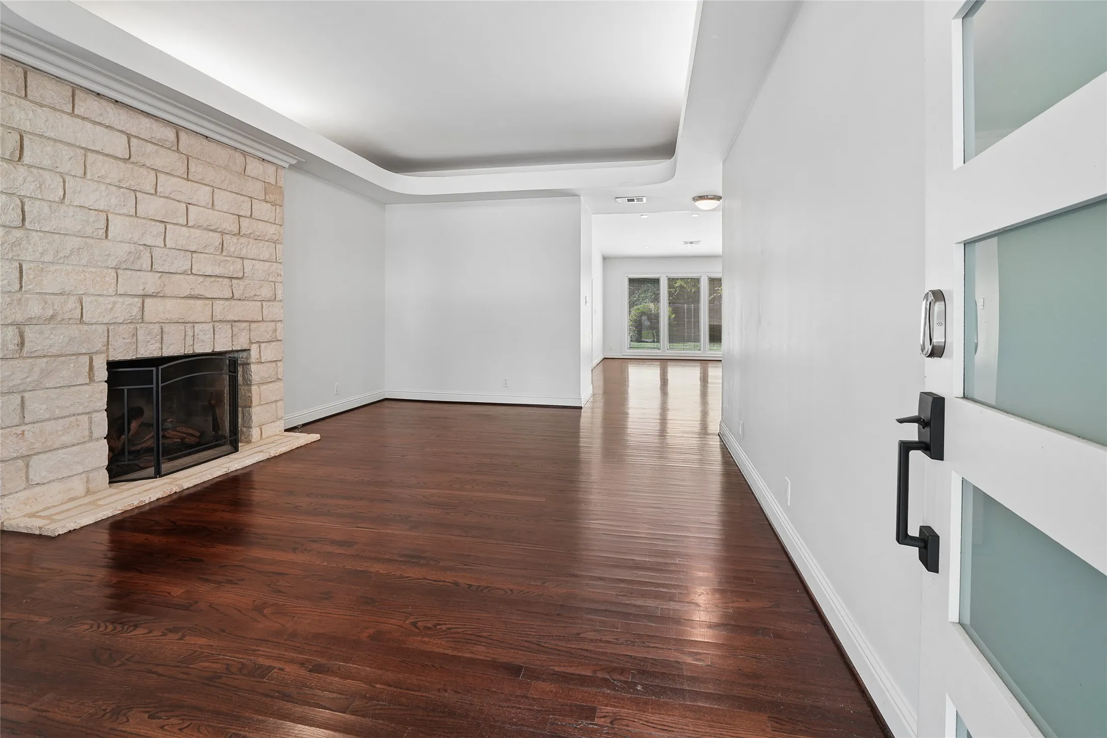 Entryway featuring a white paneled door with frosted glass inserts, dark wood-finish flooring, a stone-clad fireplace with a hearth, crown molding, and recessed lighting