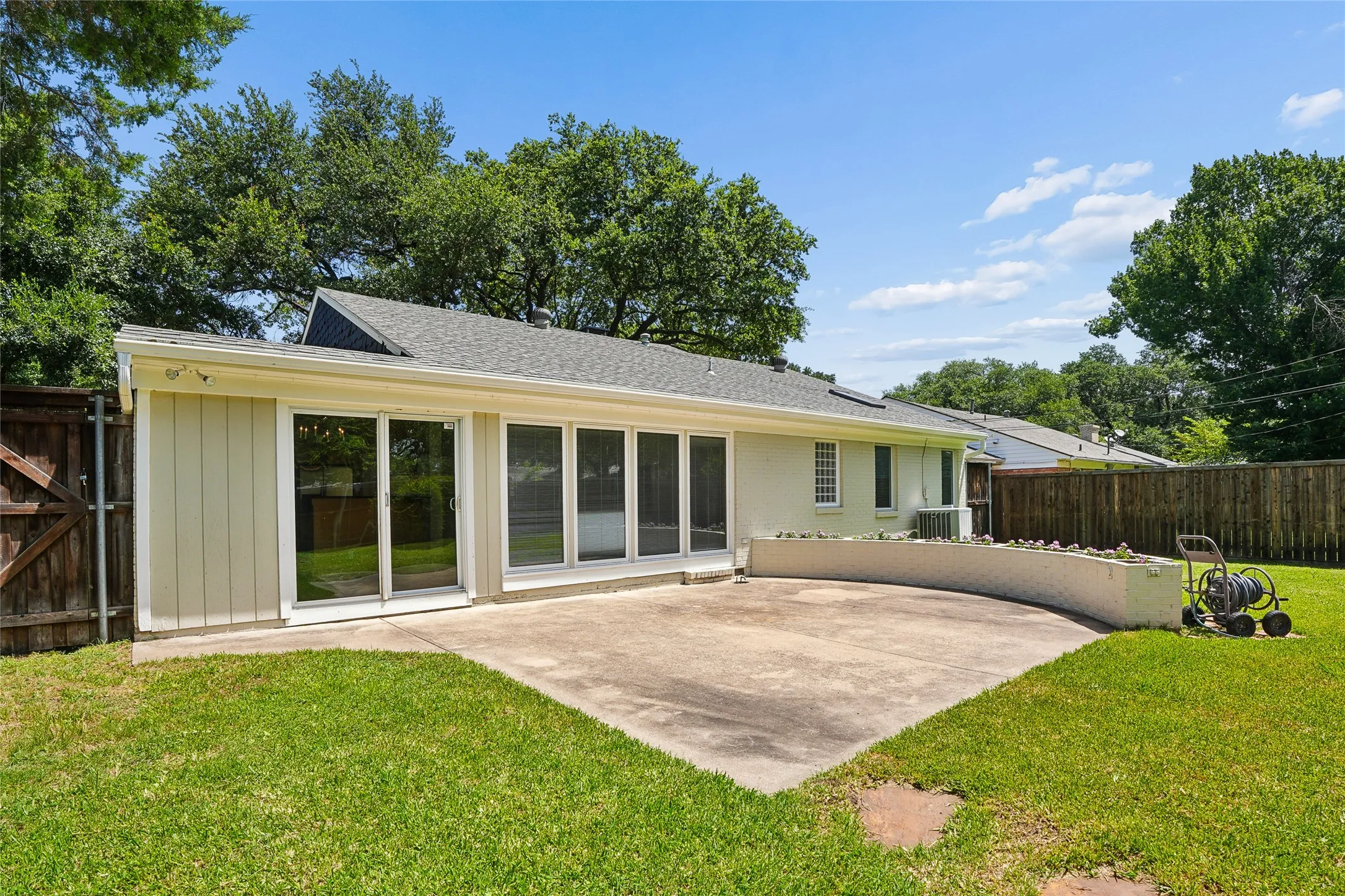 Expansive concrete patio with a curved planter box, surrounded by a manicured lawn and mature trees