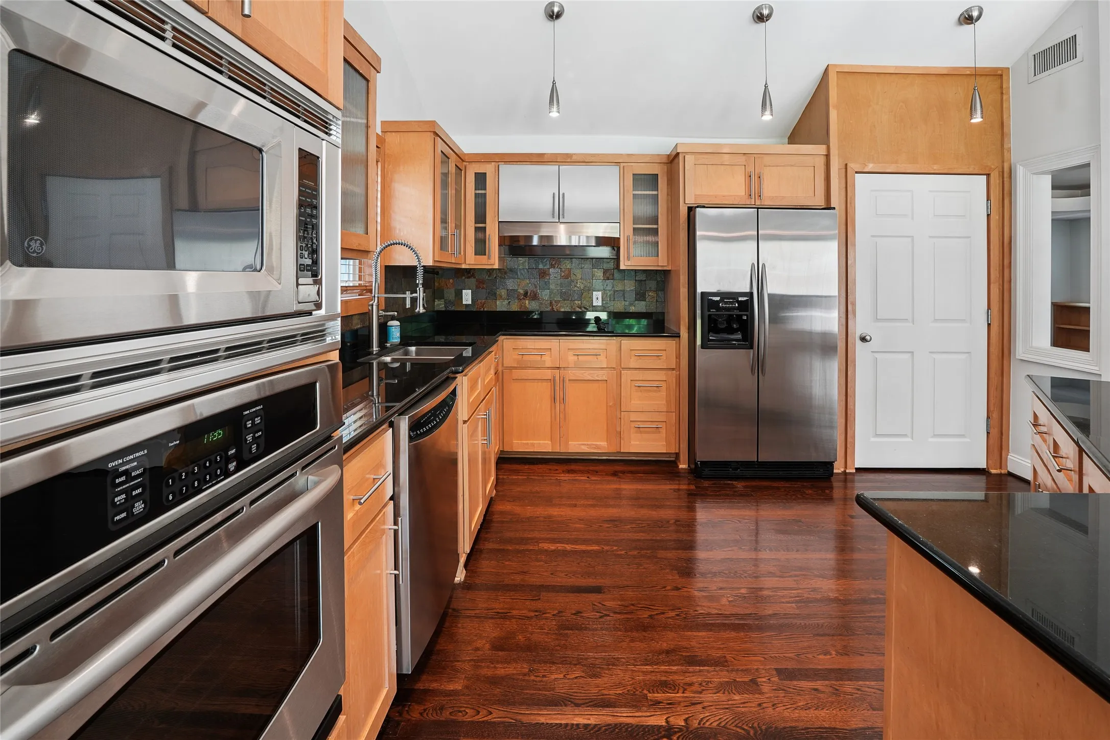 Kitchen featuring stainless steel appliances, light wood cabinetry, black countertops, and wood-finish flooring