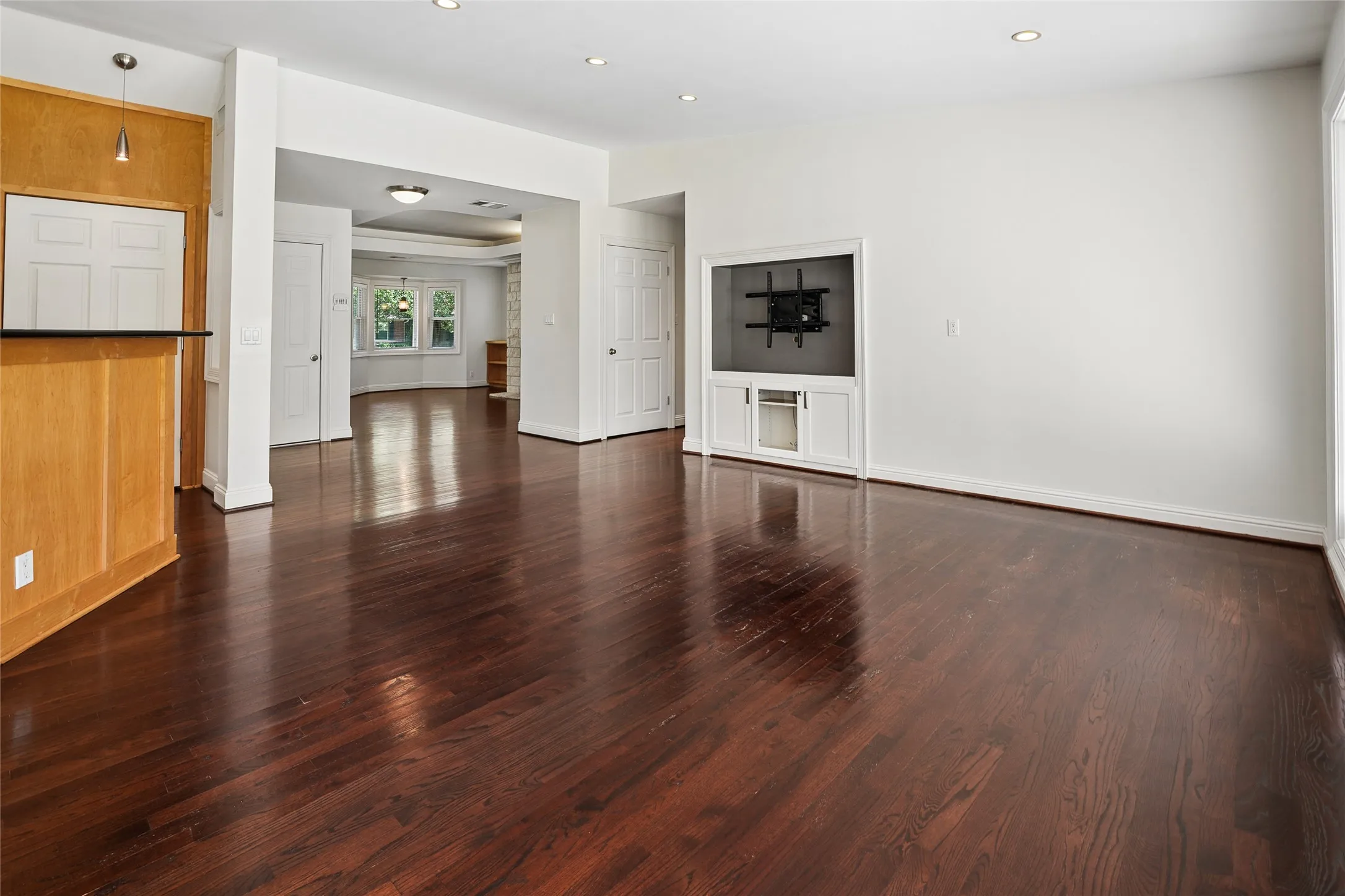 Expansive living area featuring rich wood-finish flooring, recessed lighting, and a built-in media cabinet
