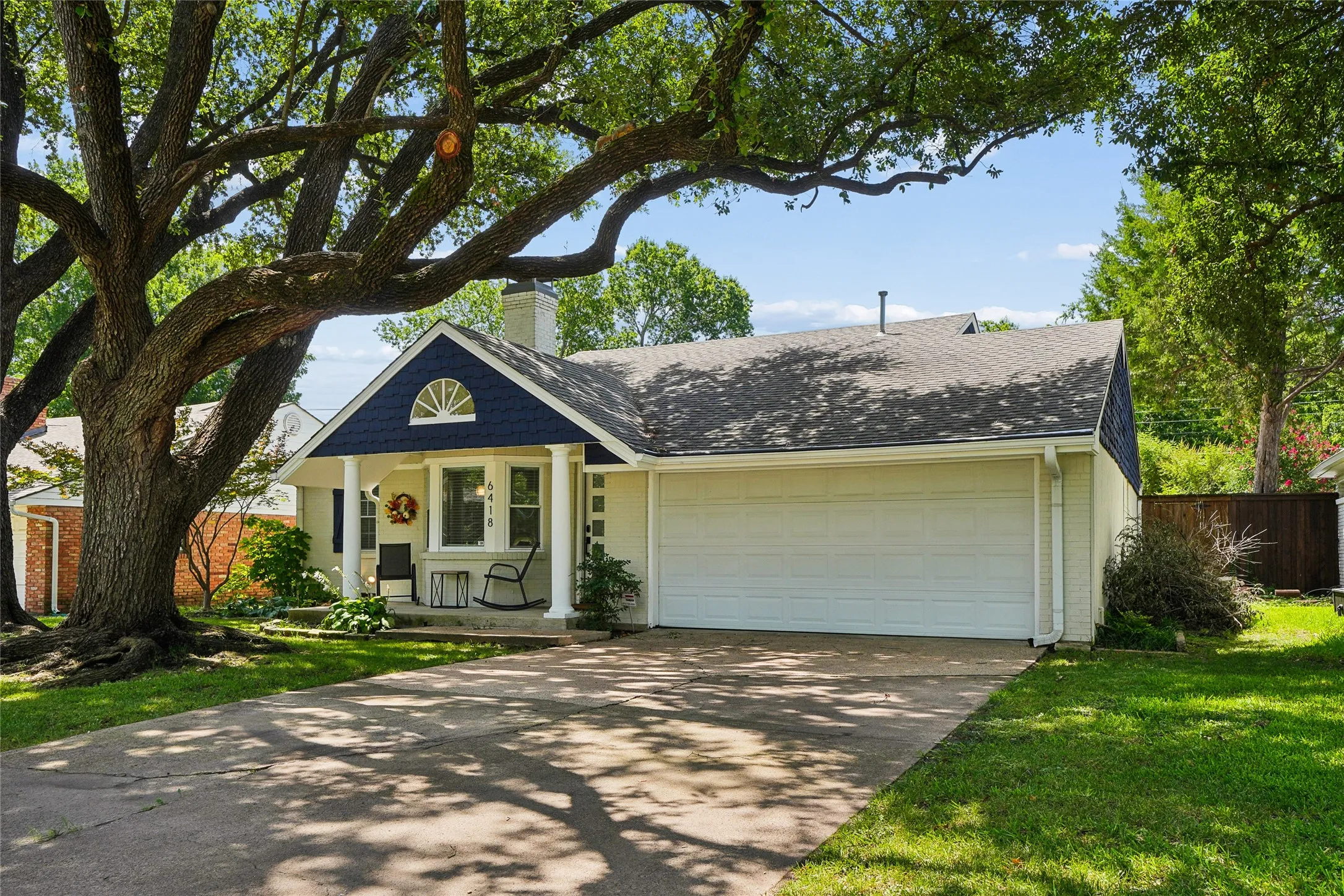 Single-story residence featuring a prominent mature tree, an attached two-car garage, and a covered front porch with white columns