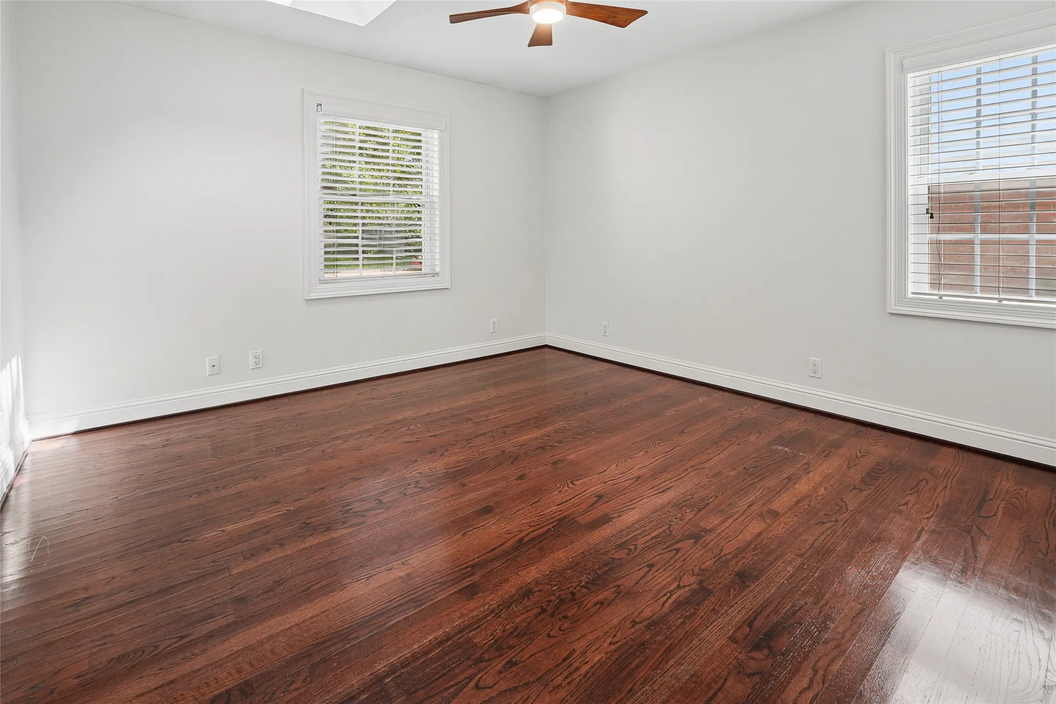 Spacious room featuring rich wood-finish flooring, white walls, and bright window treatments