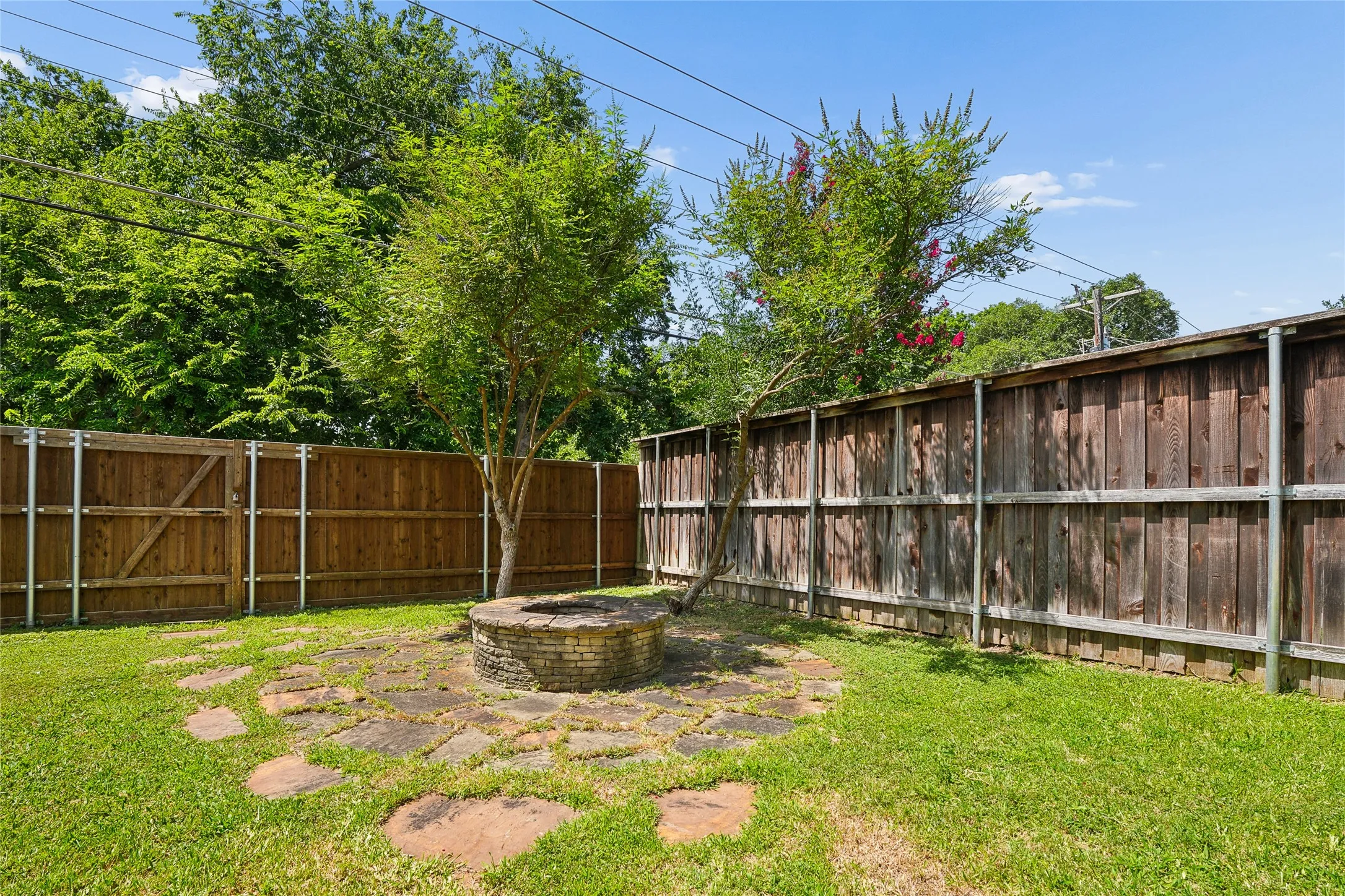 Expansive backyard featuring a central brick fire pit, flagstone patio, and mature trees