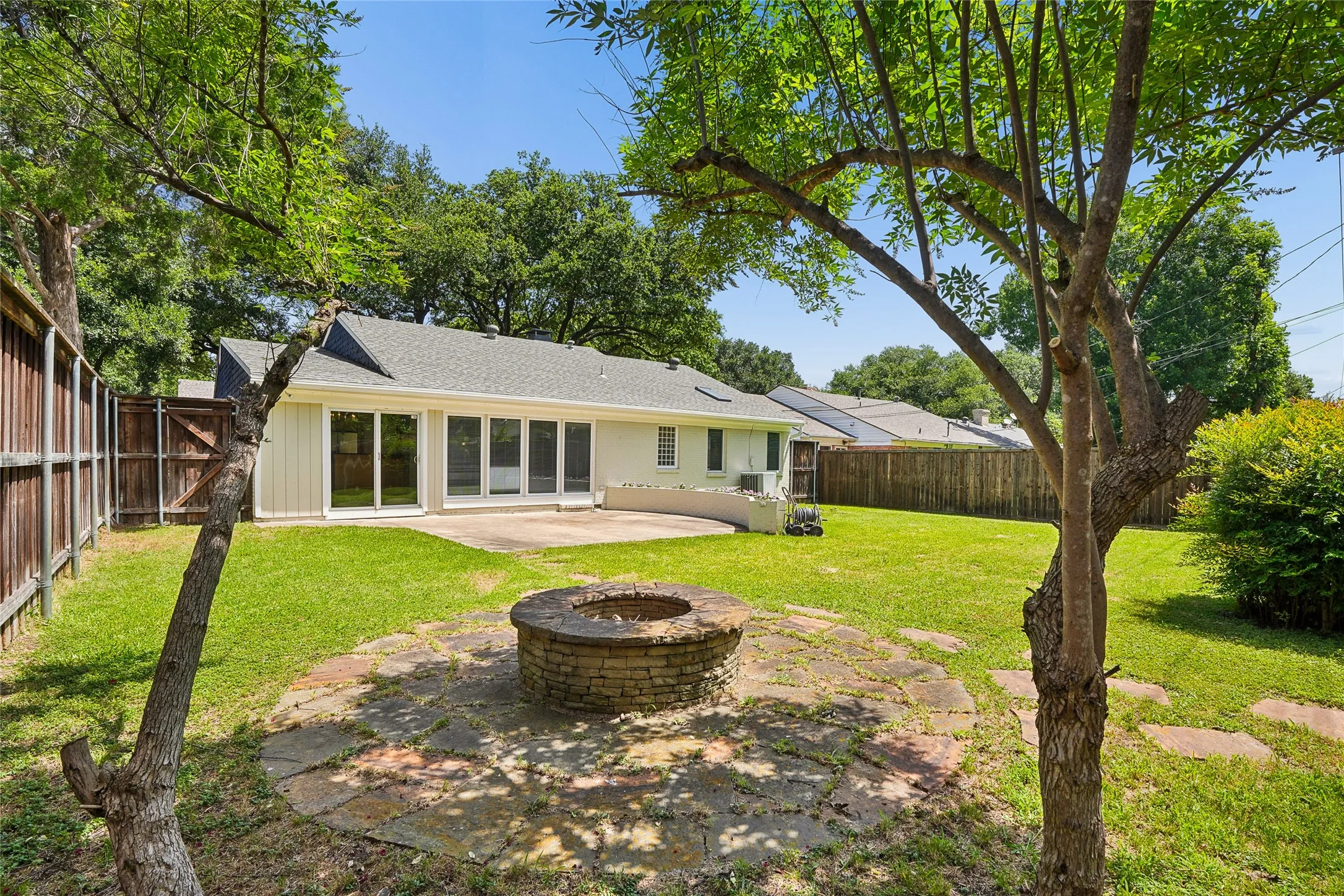Expansive backyard featuring a stone-clad fire pit, flagstone patio, and mature trees