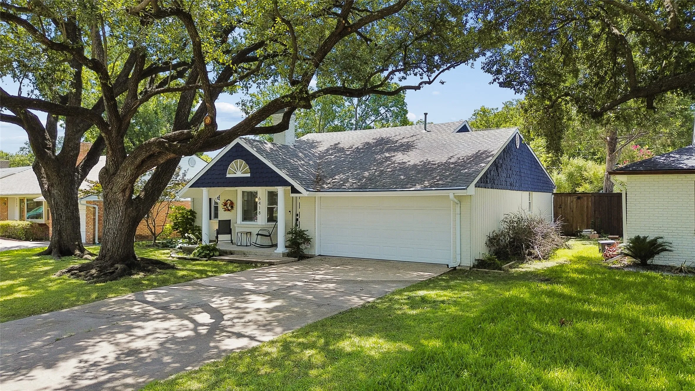 Traditional exterior featuring a charming porch entrance, attached garage, and mature tree landscaping