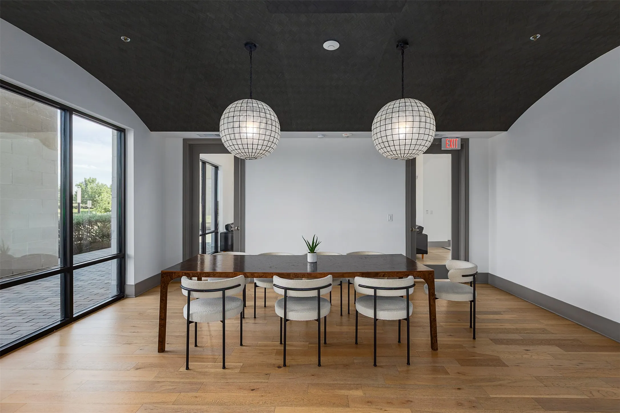 Arched ceiling with dark finish, wood-finish flooring, two spherical pendant lights, and large windows with black framing