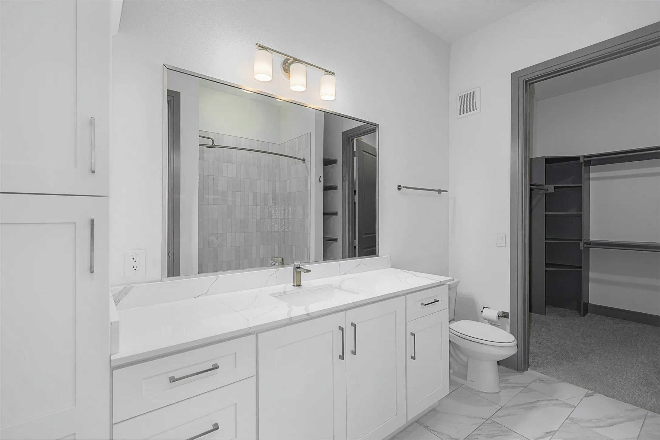 Contemporary bathroom featuring a white vanity with integrated sink, a large mirror, a three-light vanity fixture, and white cabinetry