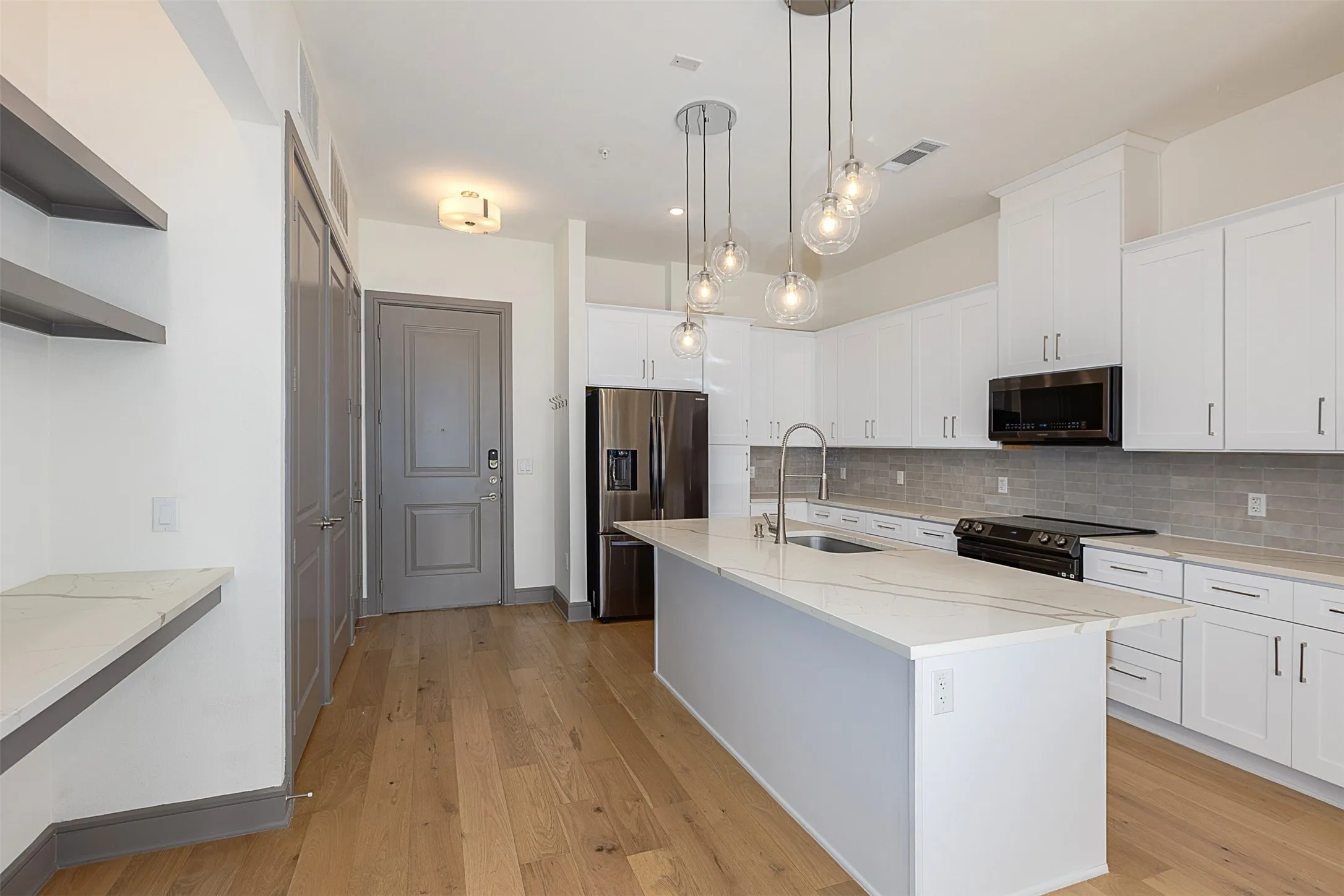 Modern kitchen with a large central island, white cabinetry, integrated stainless steel appliances, and wood-finish flooring