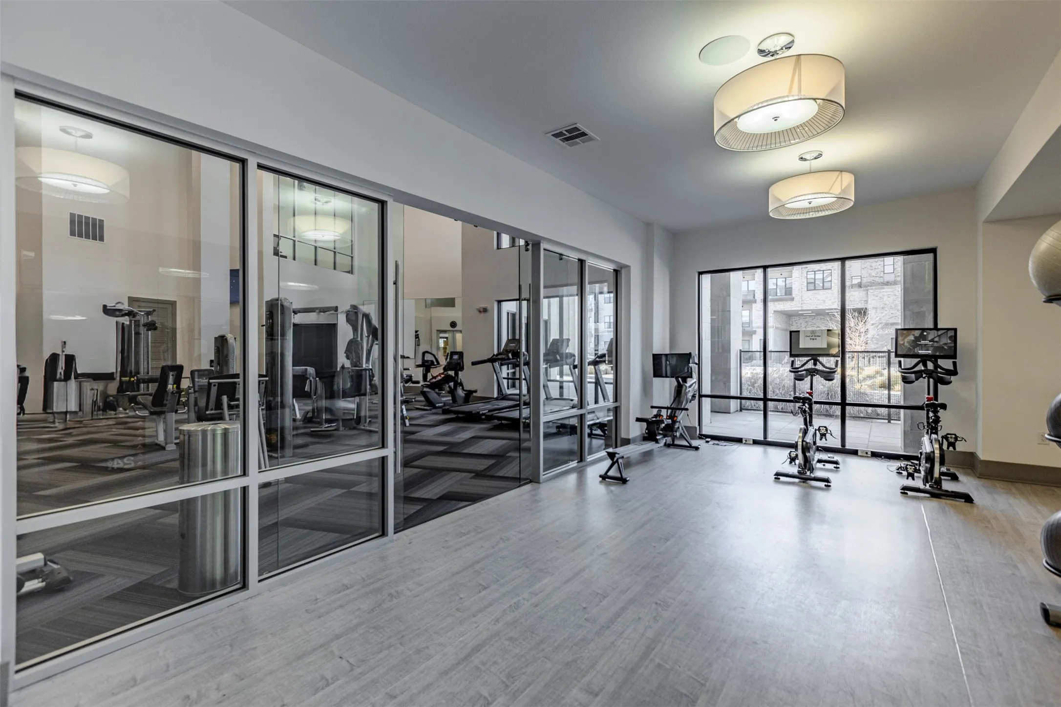 Fitness center featuring expansive floor-to-ceiling windows, wood-finish flooring, recessed lighting, and modern drum pendant light fixtures