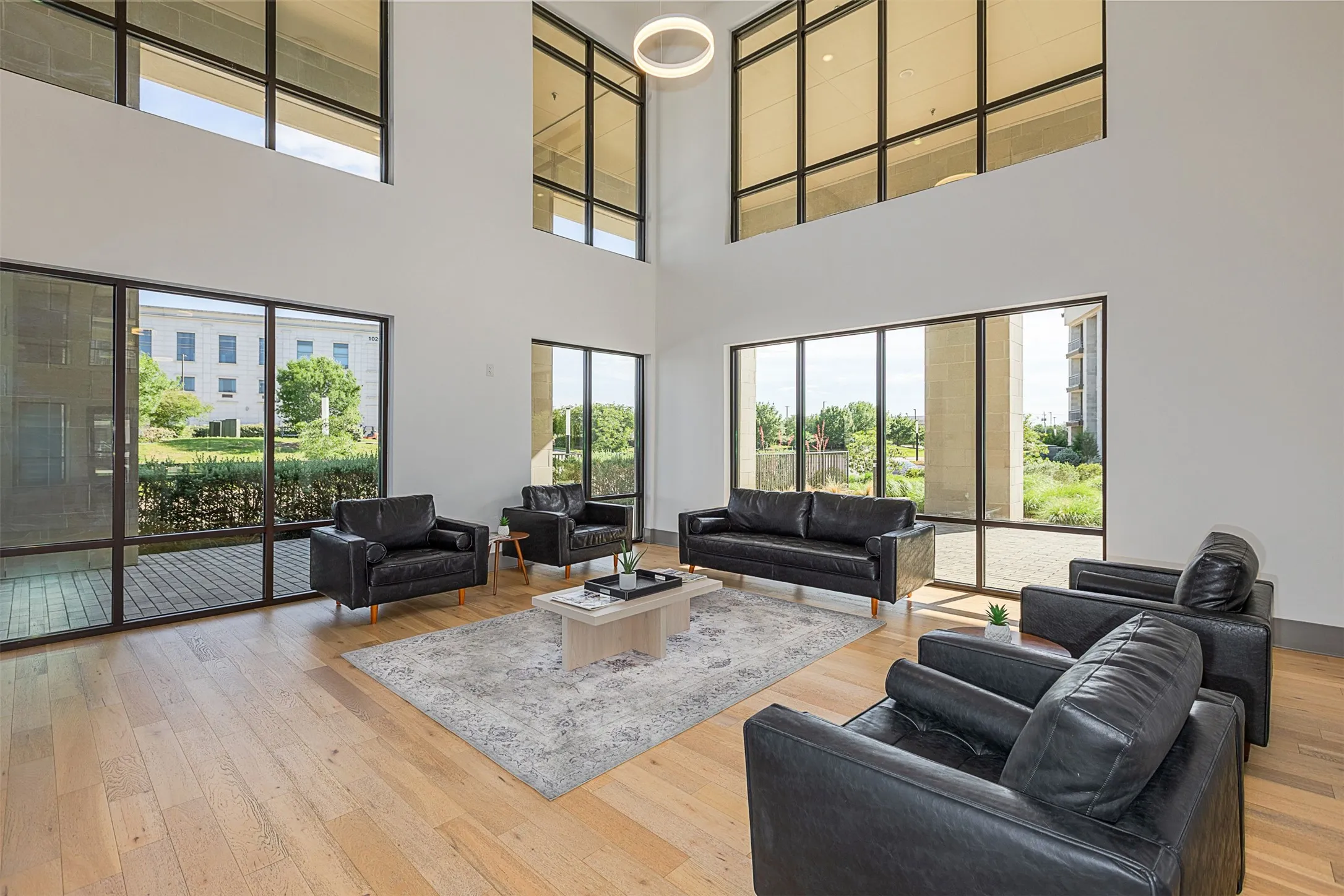 Double-height ceiling lounge area featuring expansive windows, wood-finish flooring, and a circular recessed light fixture