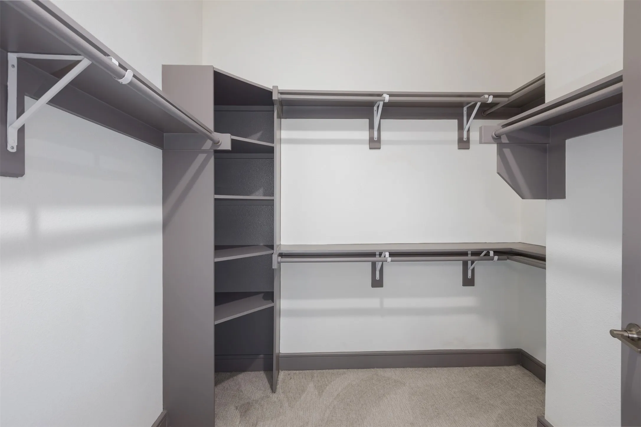 Walk-in closet featuring built-in shelving, multiple hanging rods, corner storage units, and soft gray carpet flooring
