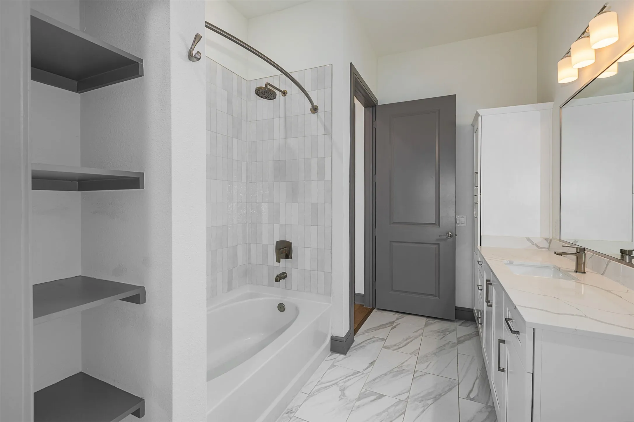 Bathroom featuring a white bathtub with tile surround, a spacious vanity with dual sinks and white cabinetry, a built-in storage cabinet, and a dark gray paneled door